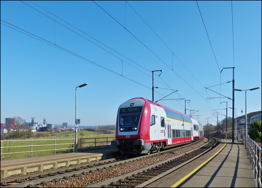 . Die RB (Regionalbunn) 6814 Luxembourg - Rodange f�hrt am 04.03.2013 p�nktlich in die Haltestelle Belval-R�dange ein, vor der Kulisse der Industriebrache Esch-Belval.

Die Industriebrache Esch-Belval erstreckt sich auf einer Fl�che von 122,7 ha westlich der Stadt Esch-sur-Alzette bis zur der franz�sischen Grenze. Dort befand sich fast ein Jahrhundert lang das integrierte Schmelz/Stahl- und Walzwerk Arbed Esch-Belval.
 
Heute stehen dort noch, als �berbleibsel der fr�hreren industriellen Aktivit�t, die beiden Hoch�fen A (rechts) und B (links), sowie die Gebl�sehalle und die M�llerei. 

Die beiden Hoch�fen A und B wurden zwischen 1965 und 1979 gebaut, sie haben eine H�he von 82, respektiv 90 Meter. Der Hochofen B war der letzte, der in Luxemburg aktiv war, sein Betrieb wurde 1997 gestoppt.

Seit 2001 stehen die beiden letzten Hoch�fen auf der Liste der klassierten Monumente in Luxemburg. 27 Millionen Euro wurden zur Verf�gung gestellt, um die Hoch�fen zu entrosten und zu sanieren. Der Hochofen A soll komplett saniert werden, w�hrend der Hochofen B nur als Silhouette stehen bleiben soll. (Jeanny)


