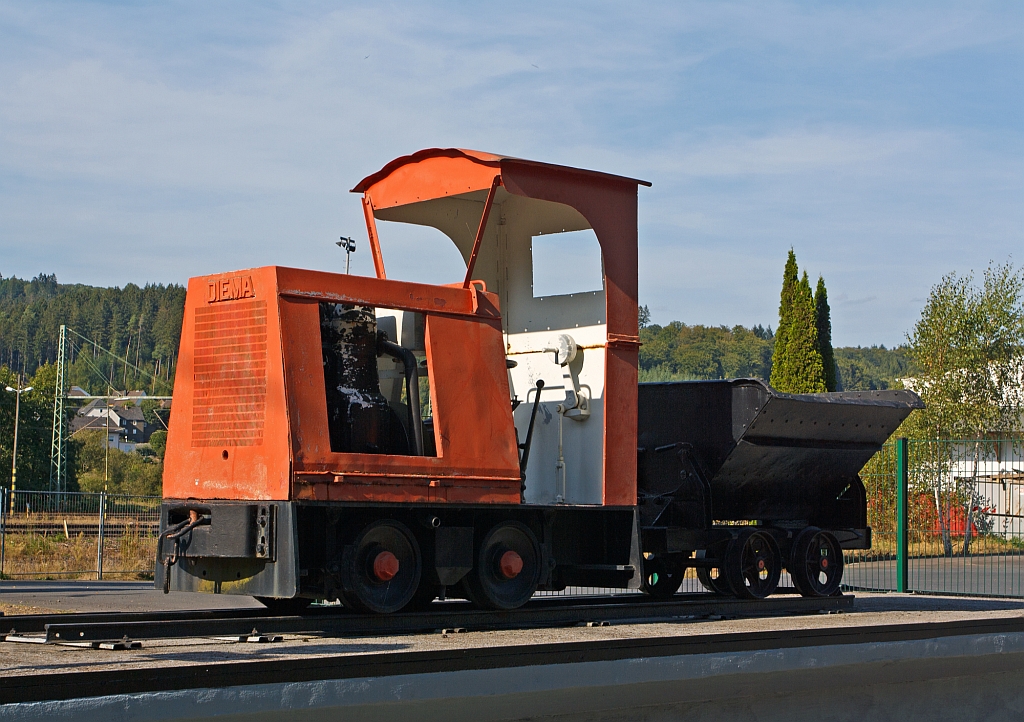 DIEMA-Lok Typ DS12 mit Lore als Denkmallok, am 09.09.2012 in Scheuerfeld (Sieg) vor dem Werktor der Dylus Industrie GmbH (ehem. BAG Feuerfest). Die 600 mm Lok wurde 1949 unter der Fabriknummer 1335 f�r Ziegelwerk Chr. Mohring-S�hne, Heiningen/W�rtt. gebaut, sie hat eine Leistung von 14 PS bei einem Eigengewicht von 2,8 t. Der Typ DS zeichnet sich aus durch den Antrieb von Motor �ber ein Kardangelenk auf ein staubdicht gekapseltes Kegelradachsgetriebe.. Diese Bauart wurde 1934 patentiert.