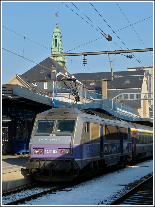 Entgegen unseren Bef�rchtungen nur noch orange farbene Loks vor dem IC 91 Vauban in Luxemburg zu sehen, war heute (01.02.2012) eine von Stefans Lieblings-Sybics zu Gast. Eine von den sechs BB 26000 im sch�nen  en voyage  Design zog heute den IC Vauban von Luxembourg nach Basel. Insgesamt gibt es 234 Loks dieses Typs bei der SNCF und sie l�sten zum Fahrplanwechsel am 12.12.2011 die Loks der S�rie BB 15000 (nez cass�s) vor der beiden Intercitys 90/91 Vauban und 96/97 Iris ab. 

Hier noch einige Informatinen zu der SNCF S�rie BB 26000: Die SYBIC ist vornehmlich aus Stahl gefertigt und besitzt aufgrund ihres futuristisch-kantigen Designs eine sehr eigene Erscheinung. Besonders bemerkenswert mit Blick auf ihre Konstruktion ist die Tatsache, dass sie, wie bereits einige fr�here franz�sische E-Loks, so genannte Monomoteur-Drehgestelle besitzt, in denen jeweils nur ein gro�er Fahrmotor �ber eine nachgeschaltete Getriebeeinheit alle Achsen des jeweiligen Drehgestells antreibt. Die Zugkraft�bertragung zwischen Lokkasten und Drehgestellen erfolgt �ber tief liegende Zug- und Druckstangen, w�hrend die Prim�rfederung auf Schraubenfedern und die Sekund�rfederung auf Gummi-Stahl-Bl�cken beruht. Die Kraft�bertragung vom jeweiligen Fahrmotor bzw. vom Verteilergetriebe auf die Rads�tze erfolgt �ber Hohlwellen-Gummiringfeder-Antriebe. 

Im elektrischen Teil kommen bei der SYBIC auf GTO-Thyristoren basierende Traktionsstromrichter zur Anwendung, welche fl�ssigkeitsgek�hlt sind. Diese arbeiten mit einer Zwischenkreisspannung von 1,5 kV Gleichstrom und k�nnen somit w�hrend des Betriebs im franz�sischen Gleichstromnetz ohne weiteres direkt aus der Oberleitung gespeist werden. Im Wechselstromnetz ist ihnen der Haupttransformator vorgeschaltet. 

Auf dem Dach sind zwei unterschiedliche Stromabnehmer angebracht, jeweils einer f�r Gleichstrom (mit vier Schleifleisten) und Wechselstrom (mit zwei Schleifleisten). F�r die Bedienung stehen dem Lokf�hrer eine einfache manuelle Zug- und Bremskraftsteuerung, das so genannte  dispositif de vitesse impos�e  (eine Geschwindigkeitssteuerung �hnlich der deutschen AFB, aber ohne Koppelung mit der pneumatischen Bremse) und als Hilfe f�r den Betrieb im 1,5-kV-Netz eine Leistungsbegrenzung zur Limitierung der Stromaufnahme zur Verf�gung. Bedienelemente f�r direkte und indirekte Bremse sind ebenfalls vorhanden. Die SYBIC besitzt Bordger�te f�r die Zugsicherungssysteme RS bzw.  Crocodile  und KVB. 

Die BB 26000 ist unter dem Kunstnamen  SYBIC  gut bekannt, dieses wurde aus  synchrone  f�r die Synchronmotoren und  bicourant  f�r die Zweisystemf�higkeit gebildet. (Jeanny)
