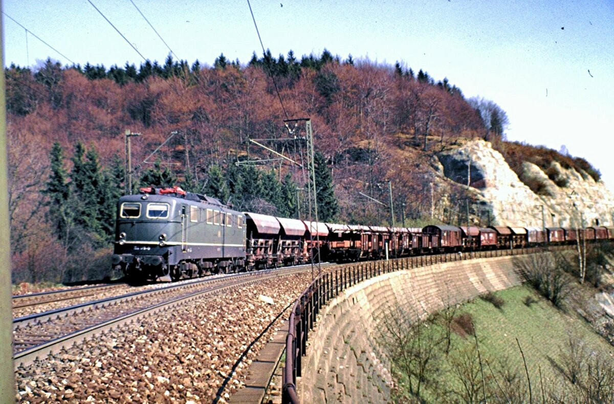 150 179-0 mit einem Schüttgut-Selbstentladewagen Typ Otmm Ganzzug und auf dem Gegengleis der hintere Teil eines gemischten Güterzuges ohne Schubhilfe auf dem Mühltalfelsendamm der Geislinger Steige am 23.04.1982.