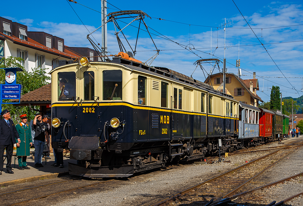 
50 Jahre BC - MEGA STEAM FESTIVAL der Museumsbahn Blonay–Chamby:
Bevor wir nach Vevey herunter „surften“...
Konnten wir noch im tollen Morgenlicht den wunderschöne Gelenktriebwagen ex MOB DZe 6/6 2002, bzw. FZe 6/6 2002 bestaunen und fotografieren. Hier steht er am 21.05.2018 im Bahnhof Blonay mit einem Zug zur Abfahrt zum Museum bereit.

Der Triebwagen Gepäck- und Postabteil wurde 1932 von SIG unter der Fabriknummer 3703 gebaut, der Elektrische Teil ist von BBC. Der Gepäcktriebwagen war bis 1996 im Einsatz und wurde dann in der Remise Gstaad Abgestellt und gammelte vor sich hin, bis er im Juli 2008 zur Museumsbahn Blonay–Chamby ging.

Die MOB (Montreux–Berner Oberland-Bahn) beschaffte für die Bespannung des “Golden Mountain Pullman Express” die beiden zweiteiligen Gelenktriebwagen FZe 6/6 2001 und 2002 (MOB-intern immer „Lokomotiven“ bzw. „Gepäcklokomotiven“ genannt). Nachdem der Expresszug schnell wieder eingestellt wurde (vor der Lieferung), fanden die beiden Gelenktriebwagen ein neues Betätigungsfeld im schweren Schnellzug- und Güterzugverkehr bzw. bespannten Sonderzüge mit den bei der MOB verbliebenen Salonwagen.

Riesig sind sie, mit ihren immerhin 17 m Länge, sind diese Gelenktriebwagen eine eindrucksvolle Erscheinung. Bis zur Einführung der Baureihe GDe 4/4 6000, also rund fünfzig Jahre lang, waren sie außerdem mit ihren rund 1.000 PS die leistungsstärksten Gleichstrom-Lokomotiven der Schweiz. 

Es war auch wie hier im Bild üblich das beide Stromabnehmer angehoben sind, da wegen der relativ geringen Spannung sehr hohe Stromstärken erforderlich sind.

Die ursprüngliche Bezeichnung war „FZe 6/6“ (Triebwagen mit Gepäck- (F) und Postabteil (Z)) wurde später in „DZe 6/6“ geändert. Eine solche Umzeichnung fand europaweit irgendwann nach dem 1. Januar 1962 statt, sie entsprach dem RIC-Reglement (Regolamento Internazionale Carrozze, ein Übereinkommen über die gegenseitige Benutzung der Personen- und Gepäckwagen im internationalen Verkehr). 

Die beiden Fahrzeuge 2001 und 2002, trugen nie irgendwelche Wappen oder Namen, sie behielten allerdings bis heute die Pullman-Lackierung in dunkelblau/crème mit gelbem Seitenstreifen

TECHNISCHE DATEN:
Fahrzeugbezeichnung: DZe 6/6 bzw. (FZe 6/6)
Anzahl Fahrzeuge: 2  (2001 und 2002)
Inbetriebsetzung: 1932
Spurweite: 1.000 mm
Achsanordnung: Bo'Bo'Bo' 
Dienstgewicht: 62,8 t
Länge über Kupplung: 17.000 mm
Kastenlänge: 2 x 7.850 mm
Fahrzeughöhe: 3.550 mm
Fahrzeugbreite: 2.700 mm
Drehgestellabstand: 2 x 5.500 mm
Achsabstand im Drehgestell: 2.300 mm
Treibraddurchmesser (neu): 945 mm
Höchstgeschwindigkeit: 55 km/h
Maximale Leistung am Rad  6 x 132 kW = 738 kW 
Getriebeübersetzung: 1:6.94
Ladefläche Gepäck- / Postraum: 10 m² / 8 m²  (4t)
Stromsystem: 900 V DC

