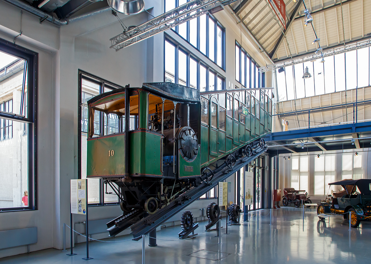 
Bhm 1/2 Zahnrad-Dampftriebwagen Nr.10 der Pilatus Bahn ausgestellt im Verkehrszentrum des Deutschen Museums in München (Theresienhöhe), hier am 16.06.2018. Leihgabe der Pilatus Bahnen.

Der Dampftriebwagen wurde 1900 von der SLM unter der Fabriknummer 1309 gebaut und an die Pilatus Bahn geliefert.

Mit Seilbahnen und Zahnradbahnen eroberten Touristen und Ausflügler am Ende des 19. Jahrhunderts die Einsamkeit der Berge. Als erster Schweizer Berg erhielt der sanfte Rigi 1875 die erste Bergbahn Europas. Nach dessen erfolgreicher Eroberung galt es dem schroffen und sagenumwobenen Pilatus am Vierwaldstätter See mit einer Bergbahn zu Leibe zu rücken. Eine besondere technische Herausforderung stellte dabei die starke Neigung der bevorzugten Trasse dar.

Eduard Locher entwickelte dafür 1888 ein Zahnstangensystem. Dank der liegenden Anordnung seiner Fischgrätenzahnstange und dem horizontalen Zahneingriff mit dem liegenden Zahnradpaar war eine Steigung von 48 % realisierbar.

Am 4. Juni 1889 dampfte der erste fahrplanmäßige Zug zum Pilatus. Er brauchte für die 4,3 Kilometer lange Strecke 70 bis 80 Minuten. Bereits 1895 reisten 40.000 Besucher per Zahnradbahn auf den Pilatus. Neun Dampftriebwagen waren dafür im Einsatz. Später kamen noch die Triebwagen 10 (1900) und 11 (1909) hinzu..

Die Triebwagen versahen größtenteils bis zur Umstellung auf elektrischen Betrieb im Jahre 1937 ihre Dienste. Mit den elektrischen Triebwagen konnte man mit weniger Personal in kürzerer Zeit mehr Gäste befördern. Bis auf die Dampftriebwagen 9 und 10 wurden die restlichen Fahrzeuge noch im selben Jahr verschrottet. Wagen 9 blieb bis 1981 als Reserve bei der Pilatusbahn und ist seitdem im Verkehrshaus der Schweiz in Luzern ausgestellt, Wagen 10 ist eine Dauerleihgabe des Verkehrshauses an das Deutsche Museum in München.

Heute fahren jährlich über 250.000 Besucher mit der steilsten Zahnradbahn der Welt auf den Pilatus, um von hier einen Blick auf die Schweizer Alpenwelt zu werfen.

TECHNISCHE DATEN:
Spurweite: 	800 mm
Achsformel:  2z
Länge über Puffer: 10.300 mm
Achsabstand der Laufräder: 7.200 mm
Leergewicht: 7,6 t 
Dienstgewicht:  13,2 t
Kohlevorrat: 500 kg
Wasservorrat: 880 l
Höchstgeschwindigkeit: 3,6 km/h (bergwärts) / 3 km/h (talwärts)
Leistung: 73 PS
Treibzahnraddurchmesser: 	409 mm
Zahnradsystem: 	Locher
Zylinderdurchmesser: 	235 mm
Kolbenhub: 300 mm
Kesselüberdruck: 12 bar
Anzahl der Heizrohre: 	130
Rostfläche: 	0,40 m²
Strahlungsheizfläche: 	2,40 m²
Verdampfungsheizfläche: 	21,0 m²
Steigung max.: 	48 %
Sitzplätze: 	35
