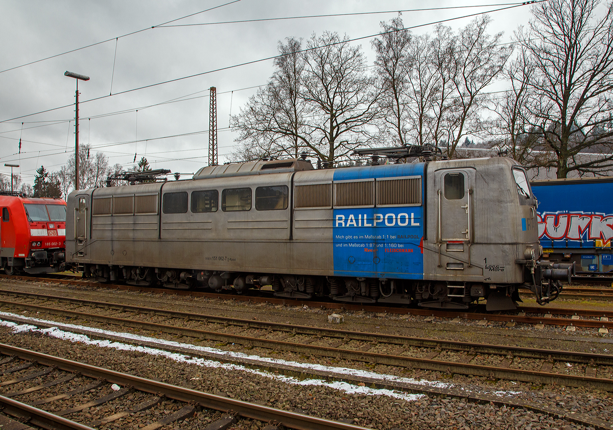 Die DB Cargo AG vermietete Railpool 151 062-7 (91 80 6151 062-7 D-Rpool) steht am 08.012022 in Kreuztal in der Abstellgruppe. 

Die Lok wurde 1974 von Henschel & Sohn in Kassel unter der Fabriknummer 31805 gebaut und an die Deutsche Bundesbahn geliefert. Bis 31.12.2016 gehörte sie zur DB Cargo AG. Zum 01.01.2017 wurden je 100 sechsachsige elektrische Altbau-Lokomotiven der Baureihen 151 und 155 an ein Konsortium aus dem Lokvermieter Railpool verkauft. Die DB Cargo mietet daraufhin 100 Loks von Railpool wieder an. Die anderen Maschinen werden dem freien Markt angeboten.

Wie auch die Werbung auf  ihr zeigt: Die Lok gibt es im Maßstab 1:1 bei RAILPOOL und im Maßstab 1:87 bei Roco und im Maßstab 1:160 bei Fleischmann. Wobei mir persönlich gefällt sie in der Farbgebung nicht gerade. Zudem könnte sie mal eine Wäsche vertragen.
