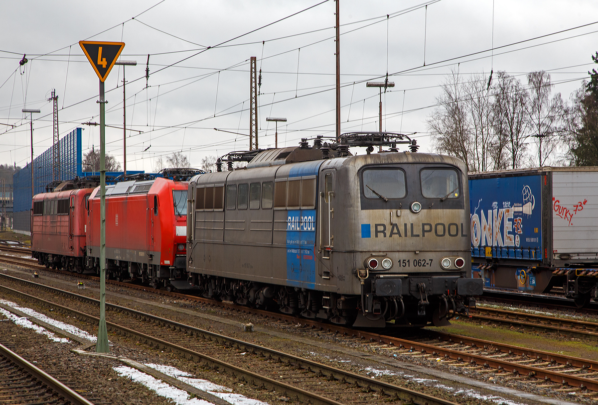 Die DB Cargo AG vermietete Railpool 151 062-7 (91 80 6151 062-7 D-Rpool) steht am 08.012022 in Kreuztal in der Abstellgruppe. Dahinter stehen noch die DB Cargo 185 002-3 und die Railpool 151 0086-6.

Die Lok wurde 1974 von Henschel & Sohn in Kassel unter der Fabriknummer 31805 gebaut und an die Deutsche Bundesbahn geliefert. Bis 31.12.2016 gehörte sie zur DB Cargo AG. Zum 01.01.2017 wurden je 100 sechsachsige elektrische Altbau-Lokomotiven der Baureihen 151 und 155 an ein Konsortium aus dem Lokvermieter Railpool verkauft. Die DB Cargo mietet daraufhin 100 Loks von Railpool wieder an. Die anderen Maschinen werden dem freien Markt angeboten.

Wie auch die Werbung auf  ihr zeigt: Die Lok gibt es im Maßstab 1:1 bei RAILPOOL und im Maßstab 1:87 bei Roco und im Maßstab 1:160 bei Fleischmann. Wobei mir persönlich gefällt sie in der Farbgebung nicht gerade. Zudem könnte sie mal eine Wäsche vertragen.
