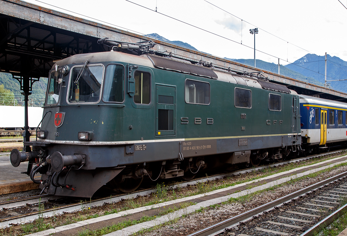 Die grüne SBB Re 4/4 II - 11161 (2. Serie) bzw. SBB 420 161-2 (91 85 4 420 161-2 CH-SBB) mit einem Einheitswagen I-Pendel (EW I), Regionalzug nach Brig, am 15.09.2019 im Bahnhof Domodossola.

Die grüne Farbe ist übrigens NICHT die Ursprungs-Lackierung der Re 4/4 II 11161, die Lok wurde 1967 in TEE Farben ausgeliefert und bekam erst nach dem Ende des TEE-Einsatzes 1981/82 die heutige grüne Lackierung.

Die Re 4/4 II ist eine vierachsige, viermotorige Lokomotive auf zwei Drehgestellen. Die Radsätze sind über Schraubenfedern am Drehgestellrahmen abgestützt. Das Drehgestell ist sekundär mit Schraubenfedern (ursprünglich Gummifedern) tief angehängt am Lokomotivkasten abgestützt. Die Zugkraftübertragung erfolgt über Tiefzugstangen von den Drehgestellen an den Lokomotivkasten.

Um einen besseren Kurveneinlauf des nachlaufenden Drehgestells zu ermöglichen, wurde zwischen den zwei Drehgestellen eine elastische Querkupplung eingebaut.

Diese Lokomotiven der zweiten Bauserie (11156–11349 und 11371–11397) haben zwei Einholmstromabnehmer und sind mit 15.410 mm (bei gleichem Drehgestellabstand) einen halben Meter länger als die Lokomotiven der 1. Serie. Die Stirnwände der Lokomotiven der 2. Serie sind etwas stärker geneigt als diejenigen der 1. Serie.

TECHNISCHE DATEN (2.Serie):
Spurweite:  1.435 mm (Normalspur)
Achsfolge:  Bo'Bo'
Hersteller: SLM / BBC / MFO / SAAS 
Dienstgewicht: 84 t (mit Klimaanlage)
Länge über Puffer: 15.410mm 
Drehzapfenabstand:  7.900 mm
Achsabstand im Drehgestell: 2.800 mm
Treibraddurchmesser:  1.235 mm
Breite:  2.970 mm
Höhe:  4.500 mm
Leistung: 4.700 kW (6.320 PS)
Stundenzugkraft: 167 kN
Anfahrzugkraft: 255 kN
Höchstgeschwindigkeit: 140 km/h
Stromsystem:  15 kV, 16,7 Hz AC