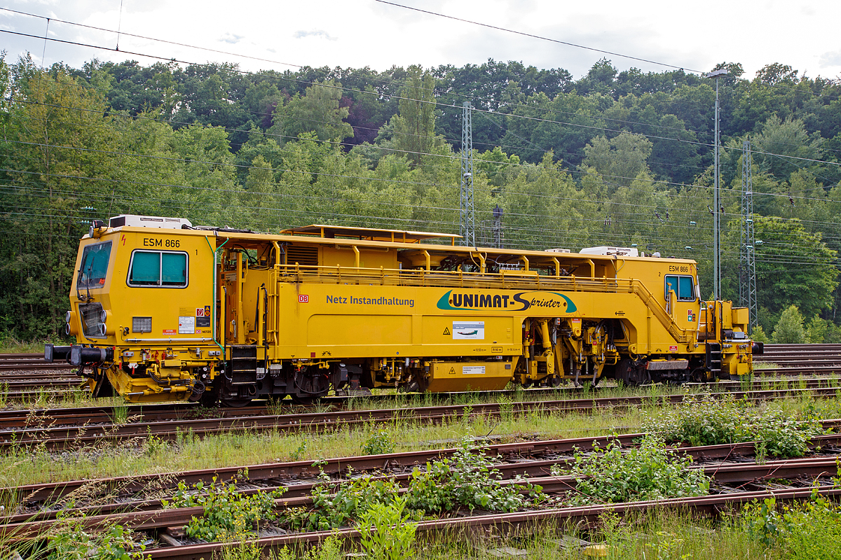 
Die Universal-Stopfmaschine Unimat-Sprinter ESM 866 der DB Netz AG (Schweres Nebenfahrzeug Nr. 97 43 52 006 17-1) steht am 04.06.2016 im Betzdorf/Sieg im Abstellbereich. Der Unimat-Sprinter ist eine von Plasser und Theurer entwickelte Stopfmaschine für Gleise, Weichen und Kreuzungen, speziell konzipiert für die rasche und präzise Behebung von Einzelfehlern. Daher auch die Abkürzung ESM = EinzelfehlerStopfMaschine.

Die Stopfmaschine (ESM – 08 – 275 / Sprinter) wurde 2000 von Plasser & Theurer unter der Fabriknummer 1169 gebaut und an die DB Netz AG geliefert.

Die typische Länge eines Einzelfehlers beträgt 9 bis 15 Schwellen, er kann sich in Einzelfällen aber bis zu 100 m weit erstrecken. Die Ursachen liegen nicht im direkten  Zusammenhang  mit  Nivellier-  und  Richtarbeiten oder Zugbelastungen, sondern vielmehr in punktuellen, scharf   abgegrenzten Schwächen im Unterbau, Frostschäden usw.
Da dieser Einzelfehler in einem völlig intakten Abschnitt liegt,  der keiner durchgehenden Behandlung bedarf, ist es viel zu aufwendig, solche Abschnitte zur Gänze zu bearbeiten. Die Behebung eines Einzelfehlers ist aber unumgänglich, da nicht  nur Gründe wie kostspielige Langsamfahrstellen dafür sprechen, sondern auch die Sicherheit des Fahrweges garantiert werden muss.

Der UNIMAT SPRINTER ist eine speziell für die Einzelfehlerbehebung entwickelte Stopfmaschine. Sie ist mit zwei Weichenstopfaggregaten mit jeweils vier Schwenkpickeln zur universellen Bearbeitung von Strecken und Weichen  ausgestattet. Das kombinierte Hebe- und Richtaggregat besteht aus einem Hebehaken, einer Richtrolle und einer Rollhebezange pro Schienenstrang. Für eine schnelle Überstellung zur Baustelle ist die Maschine mit einem hydrodynamischen Antrieb für eine Höchstgeschwindigkeit von 100 km/h ausgelegt. Flankenpflüge, die im Bereich des vorderen Drehgestells montiert sind und eine Kehrbürste am hinteren Ende der Maschine, sorgen nach den Stopfarbeiten für  die Herstellung des geforderten Schotterprofils.

Technische Daten der UNIMAT SPRINTER:
Spurweite: 1.435 mm
Achsanzahl: 4 (in 2 Drehgestellen)
Achsabstand im Drehgestell: 1.520 mm
Drehzapfenabstand: 10.500 mm
Länge über Puffer: 18.140 mm
Eigengewicht: 54t
Anhängelast: 40 t
Höchstgeschwindigkeit: 100 km/h
Zugelassen zur Mitfahrt: 4 Pers.
Kleinster befahrbarer Kurvenradius:  R 90 m      
Zugelassen für Streckenklasse: A und höher