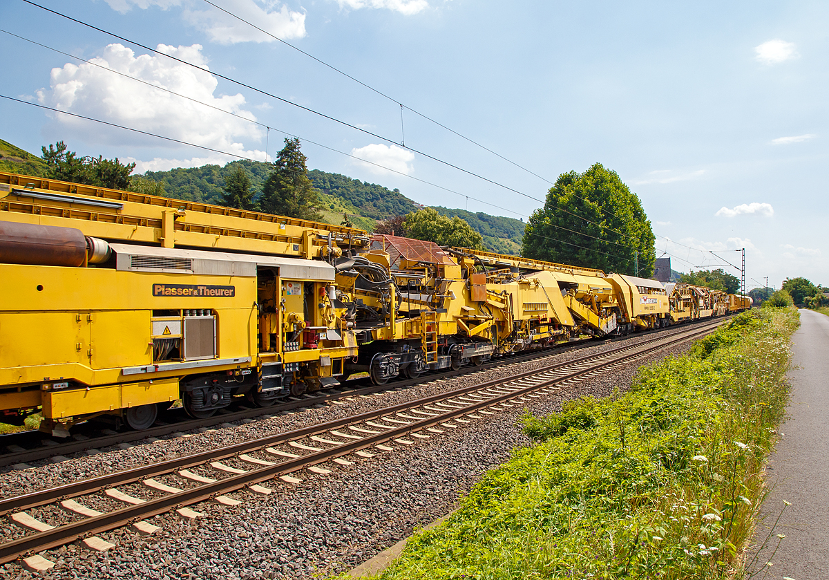 
Die Wiebe Recycling-Planumsverbesserungsmaschine mit Schotterrecycling RPMW 2002-2 am 14.07.2018 im Zugverband auf der Fahrt durch Leutesdorf,  auf der KBS 465 (Rechte Rheinstrecke) in Richtung Norden. 

Über 140 Meter lang, knapp 5 Meter hoch und gute 560 Tonnen schwer – die Gleisbaumaschine RPMW 2002-2 gehört zu den größten der Welt. Mit ihrer beachtlichen Leistung und dem umfänglichen Leistungsspektrum ist sie ein äußerst wichtiger Bestandteil des Maschinenparks der Unternehmensgruppe Wiebe.

Die Recycling Planumsverbesserungsmaschine führt verschiedene Gleisbauarbeiten durch – und das mit einer Motorengesamtleistung von über 2100 Kilowatt. Diese Kraft kommt bei Totalsanierungen zum Tragen, bei denen die RPMW 2002-2 mehrere Arbeitsschritte simultan ausführt: Die verschmutzte Schotterbettung wird ausgebaut, das abgetragene Bettungsmaterial aufbereitet, Schotter recycelt und die Unterbauplanumsschicht erneuert.

TECHNISCHE DATEN:
Hersteller: Plasser & Theurer
Baujahr, Erstzulassung: 2000
Spurweite: 1.435 mm
Anzahl der Achsen: 29, davon 12 angetrieben
Baumaschinennummer: Aushubmaschine 3369, Recyclingmaschine 3368, Antriebswagen 3367,  Stopf- u. Einschotterungsmaschine 3370
Motoren: Caterpillar 
Leistung: 2.860 PS
Gesamtlänge über Puffer: 140,90 m
Breite: 3,29 m
Höhe: 4,65 m
Gewicht: 560 t
V zul. im Zug eingestellt: 100 km/h
V max. bei Eigenfahrt: 20 km/h
Fahrradius: 120 m

Der große Unterschied zwischen Planumsverbesserungsmaschine und Bettungsreinigungsmaschinen besteht darin, dass die Planumsverbesserungsmaschine nicht nur den Schotter ausheben und recyceln kann, sondern auch einen Teil des Planums (Unterbau) ausheben (bis 1.200 mm unter SOK). Zudem kann die RPM vor der Neuschotterung (Recycling- mit Neumaterial) auch eine Planumsschutzschicht (PSS-Material) einbringen.
Der Neuschottern wird durch die Stopfeinrichtung 09-32 Stopfsatellit im Gleisbett verdichtet und das Gleis ist danach wieder mit 70 km/h befahrbar.

Hier in der Bildmitte die Planumsaushubkette:
Hat die Schotteraushubkette die Schotterschicht abgetragen, nimmt die Planumsaushubkette das verbleibende Boden- und Bettungsmaterial bis zum Erdplanum auf. Auch diese Aushubkette lässt sich stufenlos justieren, nämlich auf die gewünschte Räumbreite, Räumtiefe und Planumsquerneigung. Erneut transportieren die Förderanlagen den Aushub zur Maschinenfront, wo er auf Materialförder- und Siloeinheiten verladen wird.