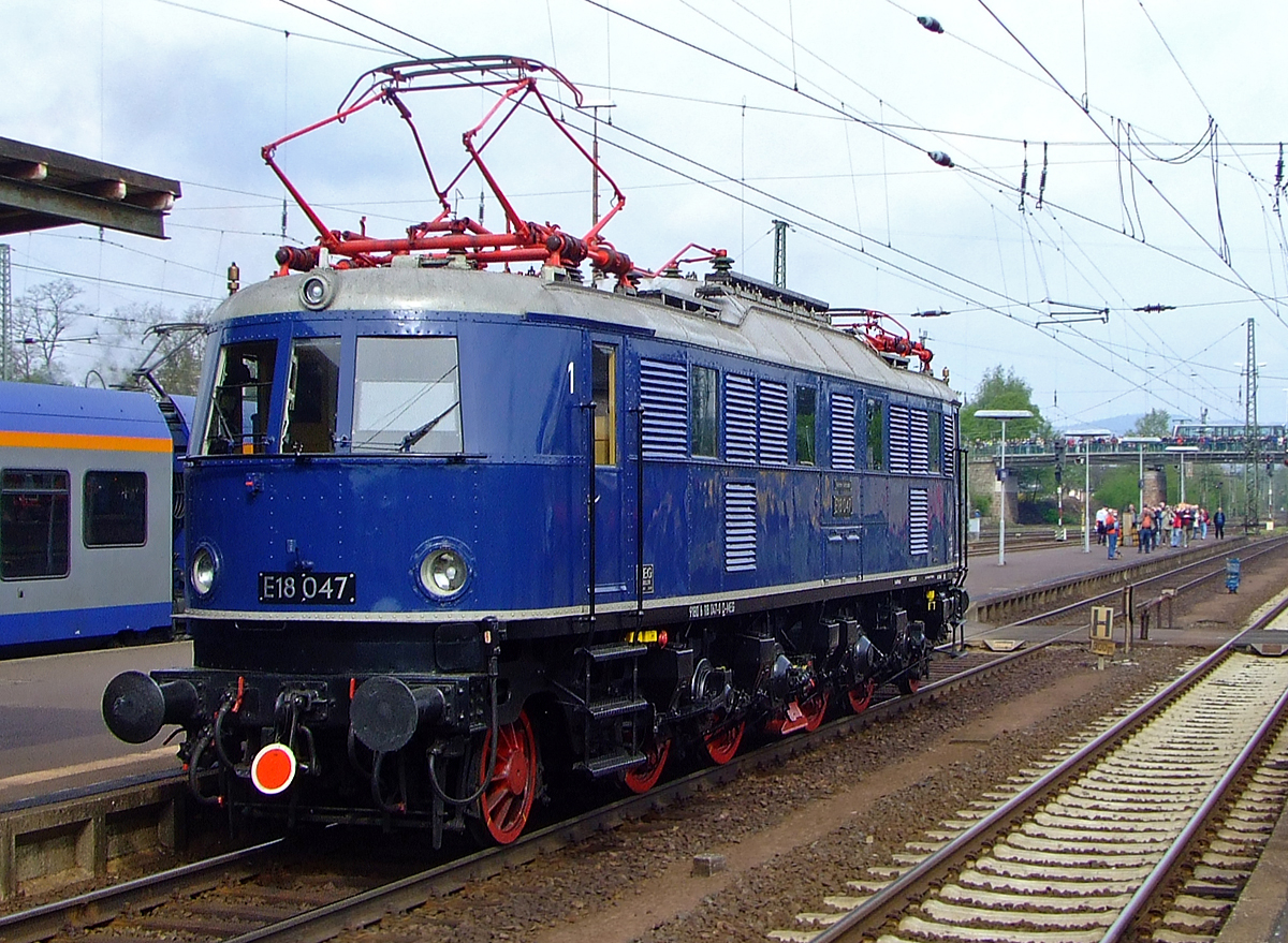 E18 047 (DB 118 047-0, eingestellt als 91 80 6118 047-0 D-MEG) fährt am 01. Mai 2010 durch den Bahnhof Bebra.

Die Schnellzug-Elektrolokomotive wurde 1939 bei AEG unter der Fabriknummer 5161 gebaut.
Die Elektrolokomotiven der Baureihe E 18 (ab 1968 DB-Baureihe 118), gehörten zu den schnellsten Elektrolokomotiven der Deutschen Reichsbahn-Gesellschaft (DRG). Sie erreichte eine Höchstgeschwindigkeit von 150 km/h. Achsanordnung ist 1 Do' 1
Die Maschine ist im Besitz des Verkehrsmuseums Nürnberg.

Lebenslauft und Bezeichnungen:
1939-1949: DRB E 18 047 (Deutsche Reichsbahn)
1949-1968: DB E 18 047
1968-1984: DB 118 047-0
1984-1997: als Museumslok DB E 18 047 (BSW-Gruppe Würzburg)
1997-2005:  E 18 047 (DB Museum)
seit 2005: E 18 047 (DB Museum Nürnberg, Außenstelle Halle/Saale, eingestellt durch die MEG - Mitteldeutsche Eisenbahn GmbH (DB Cargo Tochter)

Die Lokomotiven der Baureihe E 18 waren bestimmt zur Beförderung schwerer Schnellzüge mit hohen Geschwindigkeiten. Die Lokomotiven wurden für die neu elektrifizierten Strecken München-Stuttgart und München-Nürnberg-Leipzig-Berlin entwickelt.

Im normalen Schnellzugdienst konnten die Maschinen 935-t-Schnellzüge in der Ebene mit 140 km/h, 990-t-Züge bei 5 Promille mit 100 km/h, 600-t-Züge bei 10 Promille mit 100 km/h und 360-t-Züge bei 20 Promille mit 75 km/h befördern.

Viele Baugruppen, wie zum Beispiel die Motoren oder der AEG Federtopfantrieb, wurden von der E 04 übernommen. Der Lokkasten hingegen war eine Neuentwicklung, der den Grundsätzen der Aerodynamik und der Stromlinie Rechnung trug. Die E 18 hatte keinen genieteten, sondern einen geschweißten Fahrzeugrahmen. Die Laufachsen waren für die Laufruhe mit der jeweils ersten – verschiebbaren – Treibachse in einem AEG-Kleinow-Gestell zusammengefasst. Der Antrieb erfolgte über Federtöpfe. Jeder Radsatz wurde über den verstärkt ausgeführte Kleinow-Federtopfantriebe von hochgelagerten Gestellmotoren Typ EKB860 angetrieben. Die ursprünglichen der Stirnfront angepassten Leuchten wurden bei der DB bis auf wenige Ausnahmen durch Einheitsleuchten ersetzt. 

Bedingt durch den Zweiten Weltkrieg wurde die weitere Beschaffung der E 18 zugunsten der wichtigeren Kriegsloks E 44 und E 94 eingestellt. Bis Kriegsende wurden daher nur 53 Lokomotiven gebaut. Nach dem Krieg verblieben bei der Deutschen Bundesbahn 41 Lokomotiven, die weiterhin im Schnellzugdienst eingesetzt wurden. Obwohl die Lokomotiven sich erwartungsgemäß gut bewährten und gute Laufeigenschaften auf geraden Strecken hatten, konnten sie im Bogenlauf nicht überzeugen und dieser war durch Reibung sogar teilweise ruckartig. Die optimale Einstellung der Hohlwellen und gute Wartung verbesserten die Laufgüte der Loks. Auch der spätere Einbau von Gummi-Parabelfedern statt der Federtöpfe brachte eine Verbesserung.

Mitte der sechziger Jahre wurden die leistungsfähigen Lokomotiven durch die neu in Auslieferung befindlichen E 10 verdrängt. Die Loks wurden nun vermehrt im Nahverkehr eingesetzt, was der Schnellzuglok nicht sonderlich bekam. Die Schäden an Schaltwerk und Bremse häuften sich. In den siebziger Jahren erhielten einige E 18 die Vorrüstung für die automatische Kupplung. Es wurden sogenannte Verschleißpufferbohlen angebracht, die das elegante Aussehen der Loks nachteilig beeinflussten. 

TECHNISCHE DATEHN:
Spurweite:  1435 mm (Normalspur) 
Achsformel:  1'Do1'
Länge über Puffer:  16.920 mm
Achsabstände: 2.800 / 2.100 / 3.000/  2.100 / 2.800 mm
Treibraddurchmesser: 	1.600 mm
Laufraddurchmesser: 	1.000 mm
Dienstgewicht:  108,5 t
Radsatzfahrmasse:  18,1 t
Höchstgeschwindigkeit:  150 km/h
Stundenleistung:  3.040 kW
Dauerleistung:  2.840 kW
Anfahrzugkraft:  206 kN
Treibraddurchmesser:  1.600 mm
Stromsystem:  15 kV 16 2/3 Hz AC
Anzahl der Fahrmotoren:  4 (Gestellmotore Typ EKB86
Antrieb:  Kleinow-Federtopfantrieb
Kupplungsart: Schraubenkupplung
