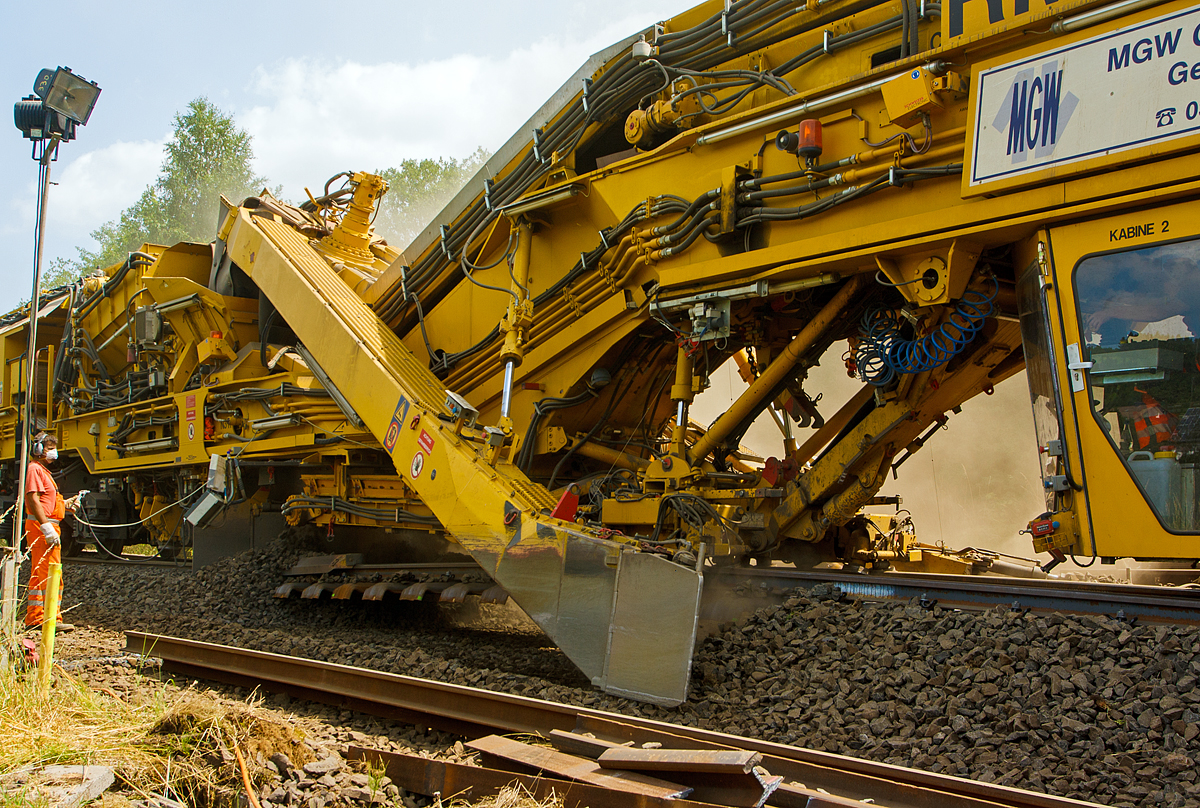 Im Einsatz auf der Hellertalbahn (KBS 462) bei Würgendorf am 15.07.2013: Die Plasser & Theurer Hochleistungs-Bettungsreinigungsmaschine RM 95-800 W, Schweres Nebenfahrzeug Nr. 99 80 9414 001-4 D-MWGB, der MGW Gleis- und Weichenbau-Gesellschaft mbH & Co. KG (Berlin). 

Detailbild im Bereich der Aushubkette, hinter ihr hängt erstmal das Gleis in der Luft, bevor wieder der aufgearbeitete Schotter darunter kommt. Zwar ist es auch möglich Neuschotter dazu zumischen, dies wurde aber hier nicht gemacht. Auch ist es möglich den Altschotter zu waschen, auch dies wurde hier nicht gemacht. Die Maschine war hier auch ohne Wasserkläranlage und Wasserwagen im Einsatz.