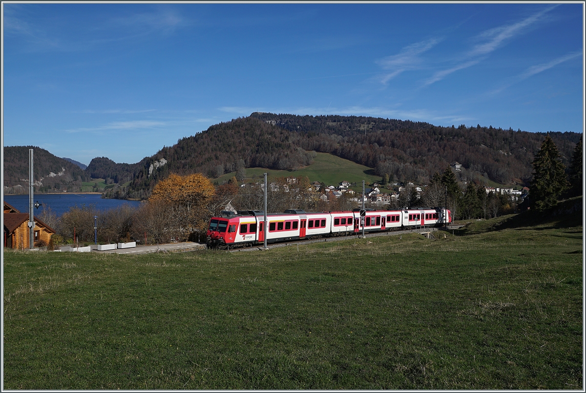 Kurz nach Les Charbonnières ist der TRAVY Regionalzug 6019 auf dem Weg nach Le Brassus. Der Zug besteht aus dem führenden Steuerwagen ABt NPZ DO TR 50 85 39-43 984-6 CH-TVYS, dem nachfolgenden Zwischenwagen B NPZ DO TR 50 85 29-43 384-1 CH-TVYS und dem schiebenden TRAVYS RBDe 560 384 (UIC RBDe 560 DO TR 94 7 560 384-0 CH-TVYS). Im Hintergrund ist der Lac Brenet zu erkennen. 

14. November 2020