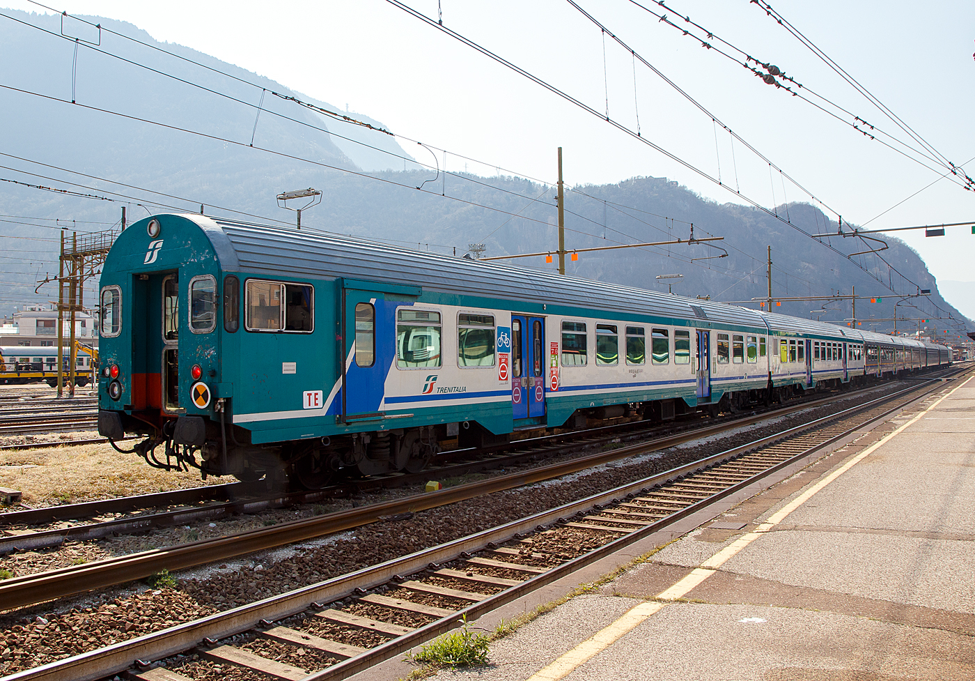 2. Klasse Reisezug- MDVC-Steuerwagen mit Gepäckabteil (MDVC steht für Medie Distanze Vestiboli Centrali, deutsch für Mittlere Entfernungen in Ballungsräumen) 50 83 82-86 807-5 I-TI der Trenitalia, der Gattung npBD und Bauart APR ( Hasenkasten -Steuerwagen) am 26.03.2022 im Bahnhof Bozen / Bolzano.

Die den Wagen handelt es sich um in Italien hergestellte Eisenbahnwaggons die speziell für den Einsatz für mittlere Entfernungen wie z.B. RE (Regionalexpress Züge). Das „TE“ (vorne unten zeigt das es sich um einen Steuerwagen vom Typ TE (Tipo TE) für E-Loks handelt.

TECHNISCHE DATEN:
Spurweite: 1.435 mm
Länge über Puffer: 26.400 mm
Breite: 2.825 mm
Höhe: 3.965 mm
Drehzapfenabstand: 19.000 mm
Achsstand im Drehgestell: 2.400 mm
Laufraddurchmesser : 860 mm (neu)
Fußbodenhöhe: 1090 mm
Eigengewicht: 40 t
Sitzplätze: 60 (2. Klasse)
Zuladegewicht: 3 t
Höchstgeschwindigkeit: 160 km/h
Bremsbauart: Freno WU-R