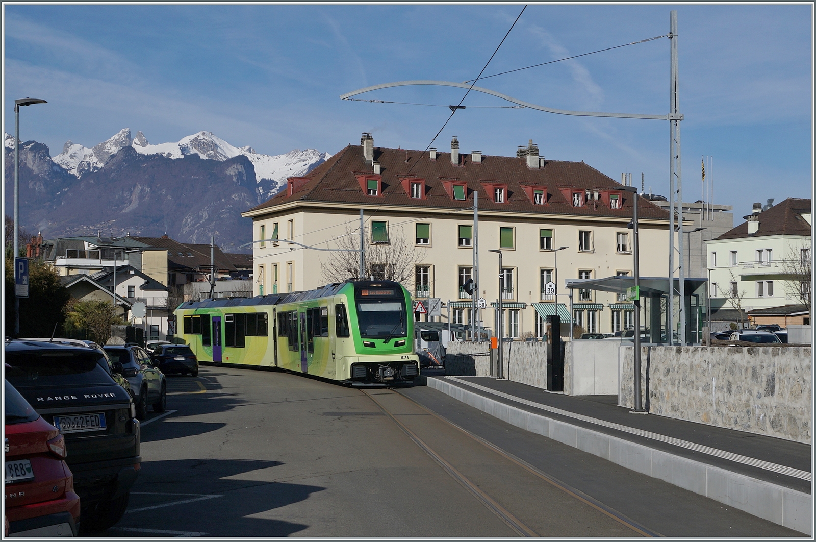 Aus der Gegenrichtung erreicht der TPC ASD ABe 4/8 471 auf der Fahrt als R71 von Aigle nach Les Diablerets den Halt Aigle Marché. Der Zug befindet sich am Halteort der alten Haltstelle Aigle Place du Marché ASD. Im Vordergrund ist der Fahrleitungsmast N° 65 zu sehen. 

9.Februar 2026