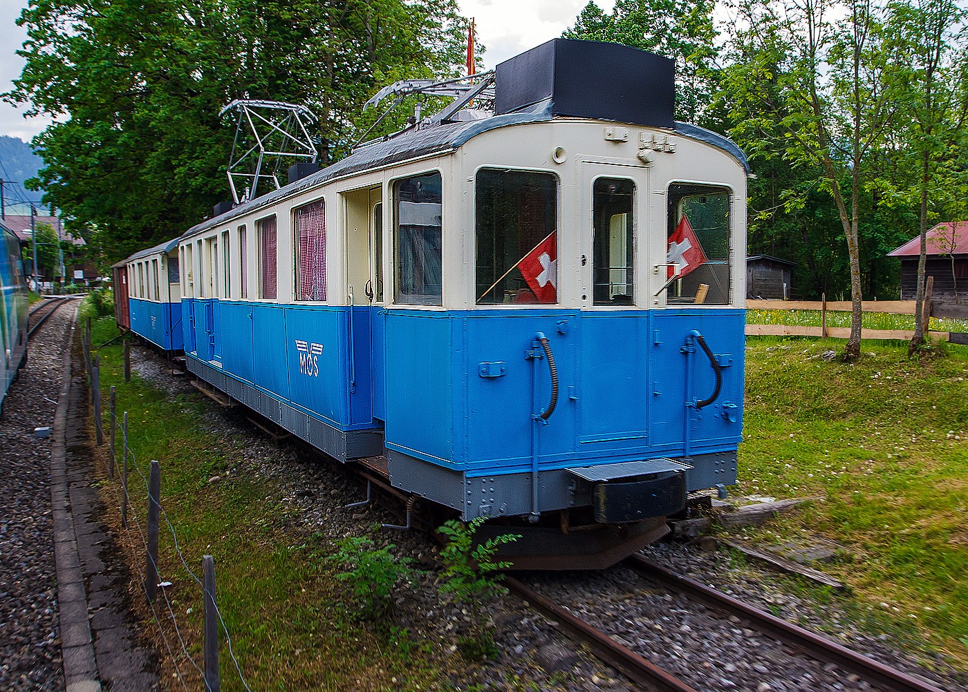 Der ehemalige MOB Triebwagen De 4/4 26 mit dem Personenwagen B⁴ 61 am 28 Mai 2012 in Saanen, aufgenommen aus fahrendem Zug. Der Zug ist seit 1994  abgestellt als Vereinslokal der Modellbahngruppe Obersimmental-Saanenland (MOS). 

Der Triebwagen wurde 1912 von SIG (Schweizerische Industriegesellschaft) in Neuhausen am Rheinfall, mit der elektrischen Ausrüstung von Alioth (Elektrizitätsgesellschaft Alioth - EGA) gebaut und als elektrischer Triebwagen mit 2.Klasse-, Gepäck- und Postabteil BFZe 4/4 26 an die MOB (Montreux-Berner Oberland-Bahn) geliefert.Mit der Abschaffung der 3. Klasse erfolgte 1956 Umbezeichnung zum AFZe 4/4 26, 1962 wurde zum ADZe 4/4 26 und 1971 zum BDe 4/4 26 (Postabteil entfiel). Bereits ab 1972 ging er zum Bahndienst, die Bänke und Gepäckträger im Abteil wurden entfernt, die Umzeichnung in De 4/4 26 erfolgte aber erst 1991 und 1994 wurde er dann an die Modellbaugruppe Obersimmental – Saanenland verkauft.

Geschichte:
Für die 1910 eingeführten Schnellzüge zwischen Montreux und Zweisimmen braucht die MOB ein geeignetes Fahrzeug, da man mit den BCFe 4/4 7–20 oft in Doppeltraktion fahren mussten. Aus diesem Grund bestellte sie diese vier Triebwagen. Weil sie nur im hochwertigen Verkehr eingesetzt werden sollten, besaßen sie nur ein 2. Klassenabteil. Dazu kam noch ein Gepäck- und ein Postabteil. Nach der Zusammenlegung der 1. und 2. Klasse im Jahr 1956, wurde das 2. Klassenabteil zum 1. Klassenabteil, und somit zum AFZe 4/4. Erst 1968/71 wurde dieses deklassiert und in ein 2. Klassenabteil umgewandelt, zugleich wurde auch das Postabteil aufgehoben, die neue Bezeichnung lautet BDe 4/4. 1979 kam es bei den letzten Triebwagen Nummer 25 und 26 zur Aufhebung des Personenabteils und die Fahrzeuge verkehrten als De 4/4. Der Triebwagen Nummer 24 wurde schon 1970 in den Xe 4/4 24 umgebaut. Der Triebwagen Nummer 25, wurde 1988 abgebrochen. Der Triebwagen Nummer 26 1994 der Modellbahngruppe Obersimmental-Saanenland übergeben, welche ihn beim Bahnhof Sannen als Vereinslokal aufstellte.

Technisches:
Die Fahrzeuge haben einen verblechten Holzkasten, der auf einem genieteten Stahlrahmen ruht. Die Kraftübertragung erfolgt über einen geschlossenen Tatzlager-Antrieb mit zweiteiligen elastischen Zahnrädern. Der Gleichstrom-Motor ist vierpolig ausgeführt und ist eigen-ventiliert. Die Übersetzung betrug bei Ablieferung 1:6,29. Bei 700 Volt an der Motorenklemme entwickelte die Motoren an der Welle eine Stundenleistung von 456 PS (336 kW). Die Steuerung der Motoren erfolgt direkt über die Fahrschalter. Auch liegt an den Motorenklemmen je nach Fahrstufe die volle Fahrleitungsspannung an. Sie besitzen zehn Fahr- und fünf Bremsstufen. Es war von Anfang an eine elektrische Widerstandsbremse eingebaut. Als Triebwagen und Zugbremse ist es eine Vakuum-Bremse der Bauart Hardy eingebaut, die auf alle vier Räder wirkt. Zusätzlich ist als Hand- bzw. Feststellbremse auf jedem Führerstand eine Handspindelbremse vorhanden. Die Fahrzeugbedienung erfolgt stehend. Die Höchstgeschwindigkeit betrug, bei der MOB erstmals ab Werk, 50 km/h. Jedes der 900 mm messende Triebrad hat einen eigenen Motor.

Das 2. Klassenabteil hatte 12 Sitzplätze, im Gepäckraum waren 9 Notsitze vorhanden, die beim Bedarf der 3. Klasse zugewiesen waren. Das Gepäckabteil war 7 m² groß und das Postabteil 6 m². Der Zugang zum Personenabteil erfolgt über eine geschlossene Plattform direkt hinter dem Führerstand und ist als Großraumabteil angelegt. Der Zugang zum andern Führerstand erfolgt über eine nur einseitig zugängliche Plattform hinter dem Führerstand. Beide Führerstände besaßen eine Stirnwandtüre. Das Post- und Gepäckabteil besaß auf beiden Längsseiten je eine innen liegende Schiebetüre. Zwischen Personen- und Gepäckabteil war eine Toilette eingebaut.

Umbauten:
Im Jahr 1926 wurden alle Fahrzeuge mit einer Sicherheitssteuerung für den Einmannbetrieb ausgerüstet. Um 1943/44 wurden beide Lyrabügel durch Scherenstromabnehmer ersetzt. Zugleich Neubemalung in blau-crème anstelle des ursprünglichen perlgrau-crème.

TECHNISCHE DATEN:
Hersteller: SIG / Alioth
Spurweite: 1.000 mm (Schmalspur)
Achsformel: Bo’Bo’
Länge über Puffer: 14.500 mm
Länge des Kastens: 13.500 mm
Drehzapfenabstand: 10.700 mm
Achsabstand im Drehgestell: 2.200 mm
Triebraddurchmesser: 900 mm (neu)
Höhe: 3.700 mm
Breite: 2.700 mm
Stundenleistung: 336 kW (456 PS)
Stundenzugkraft : 6,35 t (bei 18 km/h)
Übersetzung: 1:6,28
Höchstgeschwindigkeit: 50 km/h
Eigengewicht: 33,5  t
Fahrleitungsspannung: 850 V DC (Gleichstrom), ursprünglich 750 V DC
Stromabnehmer: 2 Scherenstromabnehmer
Sitzplätze: 12  (und 9 Notsitze im Gepäckraum) 
Gepäck- Postraumfläche: 7 m² / 6 m²
Bremsen: Hs / V / C / X
Kupplungen: Mittelpuffer mit einer Schraubenkupplungen (Zp 1)

Quellen: x-rail.ch, de.wikipedia.org
