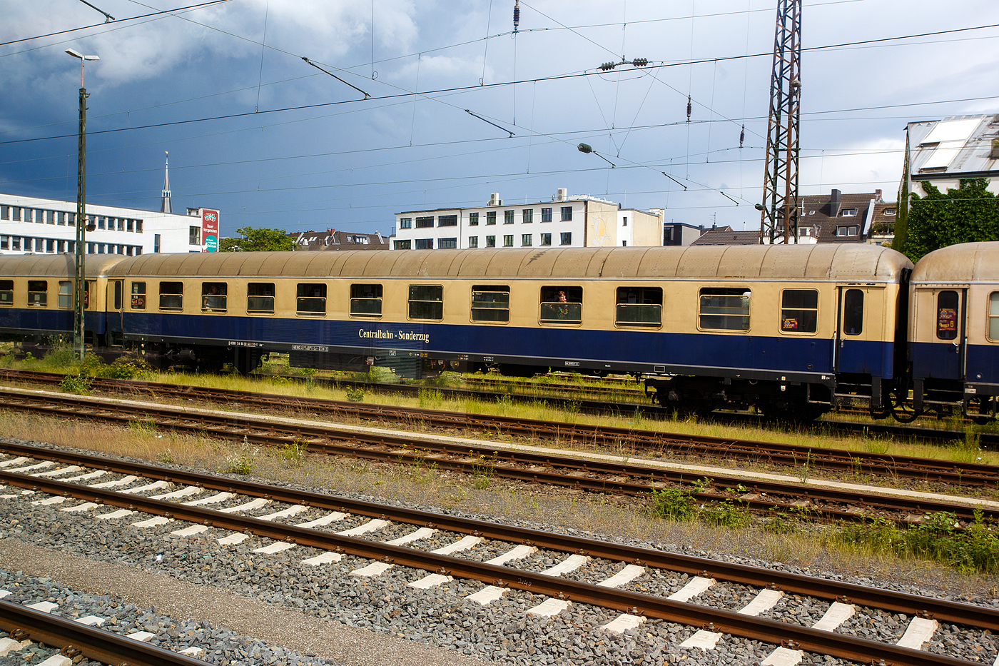 Der erste Klasse Reisezugwagen (Abteilwagen) D-CBB 56 80 10-40 130-1 der Gattung Am 208 der Centralbahn GmbH (Mönchengladbach), eingereiht im Zugverband eines mit 12 Wagen sehr langen Sonder- oder Partyzug der CBB, am 16 Mai 2024 in Köln-West, aufgenommen aus einen Zug heraus.

Der UIC-X-Wagen wurde 1959 von der Waggonfabrik Wegmann & Co. in Kassel gebaut und als DB 11 967 der Gattung A4ümg-54 an die Deutschen Bundesbahn (DB) geliefert. 1966 erfolgte der Umbau und Umzeichnung in D-DB 51 80 10-40 155-3 der Gattung Am 202, im Jahr 1986 wurde er bei Wegmann zum D-DB 51 80 03-40 130-5 Am 036 umgebaut. Im Jahr 2007 ging er als D-CBB 51 80 03-40 130-5 Am 208 an die Centralbahn.

Die Wagen der Gattung Am 208 bieten 60 bequeme Sitzplätze in zehn 6er-Abteilen der 1. Wagenklasse, zudem besitzen sie 2 WC/ Waschräume. Dieser Wagen ist für 140 km/h zugelassen und mehrspannungsfähig.

Schnellzugwagen A4ümg-54 DB
Das Bundesbahn-Zentral-Amt (BZA) Minden der Deutschen Bundesbahn (DB) entwickelte um 1952 ein Typenprogramm für 26,4 m-Fernreisezugwagen (Gruppe-53). Unter der Leitung von Dr.-Ing. Adolf Mielich entstand ein als Baukastensystem ausgelegtes Wagen-Programm. Er griff seine Entwürfe aus der Reichsbahnzeit wieder auf, zudem viele moderne Elemente wie die geschlossenen Gummiwulstübergänge und 1.000 bzw. 1.200 mm breite Übersetzfenster. Von den Vorkriegswagentypen unterschied es sich durch gerade Abteilanzahlen und symmetrische Wagenhälften, welche es ermöglichten, gleiche oder unterschiedliche Wagenklassen sowie Speise- und Packräume miteinander zu kombinieren. Nach neun Probewagen im Jahr 1952 begann 1955 die Serienfertigung. Die B4ümg-54 Reisezugwagen (1.225 Stück) boten den Reisenden der 2. Klasse erstmals nur drei Sitze pro Bank, statt bisher vier. Diese Komfortverbesserung bei dem „Reisezugwagen fürs Volk“ kam bei den Fahrgästen sehr gut an. Die erstklassige Wagenbauart A4ümg-54 (199 Stück) unterstrich beispielhaft den gestiegenen Reisekomfort jener Zeit. In eleganter, dunkelblauer Lackierung verließen die Wagen die Werke und wurden vorrangig in die F-Zugverbände der DB eingereiht. Vervollständigt wurde die Wagengruppe-53 durch die gemischt-klassigen AB4ümg-55 (357 Stück) und ab dem Ende der 1950er-Jahre durch die Halbgepäckwagen der Bauart BPw4üm-58/59 (138 Stück). Durch ihre wegweisenden Neuerungen waren die Wagen, und die aus Ihnen abgeleiteten späteren Umbauten, für die kommenden Jahrzehnte nicht aus den Reisezügen der DB wegzudenken. So verwundert es nicht, dass die letzten Wagen teilweise erst zu Beginn in den 1990er-Jahre ausgemustert wurden, oder dann ein zweites Leben im Museumsverkehr begannen.

TECHNISCHE DATEN:
Spurweite: 1.435 mm (Normalspur)
Länge über Puffer: 26.400 mm
Wagenkastenlänge: 26.100 mm
Wagenkastenbreite: 2.850  mm
Höhe über Schienenoberkante: 4.050 mm
Drehzapfenabstand: 19.000 mm
Achsstand im Drehgestell: 2.500 mm
Drehgestellbauart: Minden-Deutz 330
Leergewicht: 37 t
Höchstgeschwindigkeit: 140 km/h
Sitzplätze in der 1. Klasse: 60
Abteile: 10
Toiletten/Waschraum: 2 
Bremsbauart: KE-GPR
Energieversorgung: Achsgenerator

Die Centralbahn GmbH (Mönchengladbach) gehört zur Centralbahn AG mit Sitz in Basel. Hauptgeschäft ist die Durchführung von Sonderzugfahrten mit eigenen Fahrzeugen.