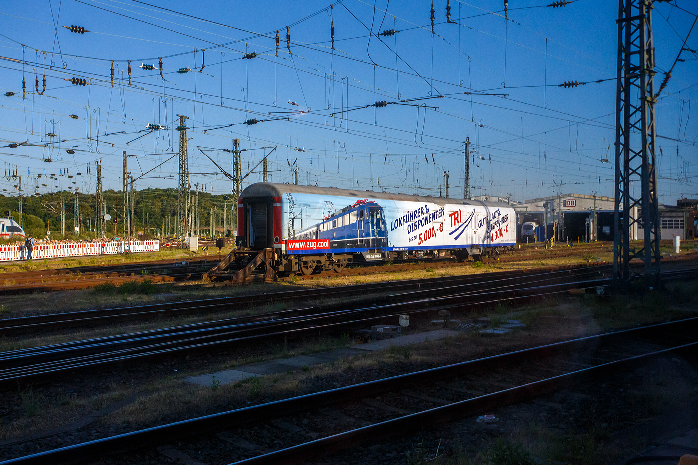Der Werbewagen D-TRAIN 50 80 22-35 929-5 der Gattung Bnrz 450.3 (Vollwerbung TRI sucht Lokführern/Disponenten und Gute Laune Zugführern) der TRI Train Rental GmbH, abgestellt beim BW Köln Bbf, hier am 01 Juli 2025 aus einem Zug fotografiert. Der Wagen ist ein n-Wagen (ex Silberling) bzw. ein lazarettfähiger 2. Klasse Nahverkehrswagen, er wurde 1970 vom AW Karlsruhe, als DB 50 80 22-35 929-5 Bnrz 724 gebaut. 2001 wurde er im DB Werk Wittenberge in die Gattung Bnrz 450.3 umgebaut. Vermutlich 2017/18 wurde er von der DB Regio an die TRI Train Rental GmbH verkauft. Die Unterbauart 450.3 verfügt im Gegensatz zu den übrigen Varianten weiterhin über eine lazarettfähige Inneneinrichtung.

TECHNISCHE DATEN:
Spurweite: 1.435 mm (Normalspur)
Länge über Puffer: 26.400 mm
Wagenkastenlänge: 26.100 mm
Wagenkastenbreite: 2.825 mm
Höhe über Schienenoberkante: 4.050 mm
Drehzapfenabstand:19.000 mm
Achsstand im Drehgestell: 2.500 mm
Drehgestellbauart: Minden-Deutz 432
Leergewicht: 33 t
Höchstgeschwindigkeit: 140 km/h
Sitzplätze: 96 in der 2. Klasse
Abteile: 3 Großräume (2. Klasse)
Toiletten: 1, geschlossenes System
Dienstraum: ja
Bemerkungen: Design OFV mit Glastrennwänden; lazarettfähig
