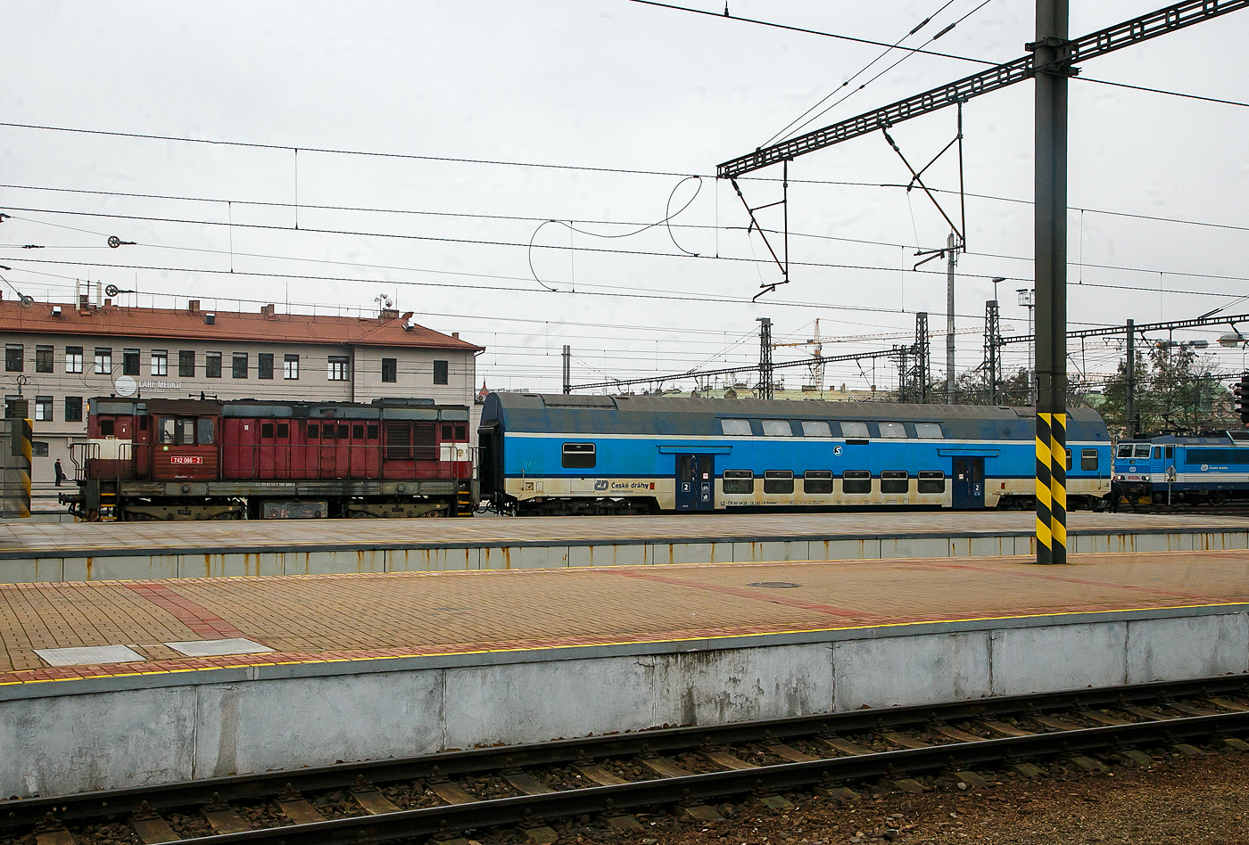 Die ČD 742 086-2 (CZ- ČD 92 54 2 742 086-2) fährt am 23.11.2022, mit dem  2. Klasse klimatisierten Doppelstock-Reisezugwagen, CD-CZ 50 54 26-18 141-6, der Gattung Bdmteeo 296 (ex CD-CZ 50 54 26-18 141-6, Bmto 292), in den Prager Hauptbahnhof (Praha hlavní nádraží) ein. Der 44 t schwere Wagen verfügt über 126 Sitzplätze, 8 Stellplätze für Fahrräder und ein geschlossenes WC-System.

Die Diesellok  Kocour   oder  Tranzisto   (Kater, Transistor):
Die ČSD-Baureihe T 466.2, ab 1988 Baureihe 742 sind dieselelektrische Güterzug- und Rangierlokomotiven der ehemaligen Tschechoslowakischen Staatsbahn (ČSD). Die Entwicklung begann 1970 mit den beiden Prototypen der BR T 475.15 (744.5). 

Das Leistungswachstum in der Motortraktion sowie die Notwendigkeit von Fortschritten bei der Erneuerung der Dampftraktion und der künftigen Typenvereinheitlichung des Motorlokparks veranlassten das Verkehrsministerium, die Beauftragung der Entwicklung und anschließenden Produktion einer neuen Lokomotive zu prüfen. Diese sollte für mittelschweren bis schweren Rangierdienst, leichteren Gleisdienst, aber auch im Güter- und Personenverkehr, bestimmt sein.

Zwei Prototyp-Lokomotiven der Reihe T 475.15 (744.5) wurden 1970 von ČKD in Praha gebaut, wurden aber von der ČSD als ungenügend abgelehnt. Dies lag hauptsächlich an ihrem Führerstand,  während die ČSD einen Turmführerstand mit guter Sicht verlangte, hatten diese Lokomotiven einen Führerstand neben dem hinteren Ende der Lokomotive, sodass die Aussicht nicht sehr zufriedenstellend war. Die Maschinen der Baureihe T 475.15 wurden daher verworfen und stattdessen die neuen Lokomotiven der Baureihe T 466.0 (735) produziert. Die Produktion erfolgte ab 1972 im Turčianské strojárny in Martin. 1973 begann bei ČKD Prag die Produktion neuer Lokomotiven der Reihe T 448.05 (740.5), die für den Bedarf großer Industrieunternehmen und für den Export bestimmt waren. Die Produktion von Lokomotiven T 466.0 (735) bei TS Martin verzögerte sich noch, die Entwicklung von Lokomotiven der Baureihe T 466.1 blieb erfolglos, außerdem war geplant, die Produktion von Lokomotiven bei TS Martin einzustellen und das Werk auf die Waffenproduktion zu konzentrieren . Auch die bereits produzierten T 466.0 (735) Maschinen waren im Betrieb sehr unzuverlässig. Die Situation in der Flotte der ČSD-Motorlokomotiven ist daher unerträglich geworden. Deshalb hat sich die ČSD eine Notlösung einfallen lassen: 1976 bestellten sie bei der ČKD 60 neue Lokomotiven der Baureihe T 466.2 (742), die genau aus den Industriemaschinen der T 448.05 (740.5) entstehen sollten. Die Serie, die bereits seit drei Jahren in der Industrie im Einsatz war, mit zudem sehr guten Ergebnissen. Die Liste der erforderlichen Umbauten war recht lang: Gewichtsreduzierung, Umbau des Triebwerks, Einbau einer Zugsicherung, Umbauten im elektrischen Teil, Umbau der Bremsen.1977-78 wurden 60 Lokomotiven der 1. Serie gebaut geliefert und die neuen Maschinen wurden fast sofort auf CSD in Betrieb genommen. Die 2. Serie folgte sofort und eine weitere danach. Die Produktion der Lokomotiven T 466.2 (742) für die ČSD endete mit der 9. Serien im Jahr 1986; insgesamt erwarb ČSD 453 dieser Lokomotiven. Während der langjährigen Produktion gab es mehrere partielle 

Modifikationen an der Konstruktion der Maschine – ab der 2. Serie mehrgliedrige Lenkung und Zugkraftwähler, ab der 3. Serie eine Knickbrücke seitlich am kürzeren Vorbau, ab der 6. Serie wurden Jalousien auf dem Dach der Lokomotive installiert und ab der 7. Serie neue Fahrmotoren. 41 Lokomotiven wurden für den Bedarf der Industrie geliefert, Maschinen auf Basis der Baureihe T 466.0 ČSD wurden auch nach Vietnam und Bangladesch geliefert. Nach der Produktion von Lokomotiven T 466.2 (742) für ČSD erfolgte 1987-88 die Produktion von abgeleiteten Lokomotiven T 466.3 (743) für Adhäsionsbetrieb auf Steilstrecken.

TECHNISCHE DATEN der BR 742, ex T 466.2:
Hersteller: ČKD Praha
Baujahre: 1977 bis 1986
Hergestellt e Anzahl: 453 für die ČSD (in 9 Serien), 41 weiter für andere
Spurweite: 1.435 mm (Normalspur)
Achsfolge: Bo'Bo'
Länge über Puffer: 13.580 mm ( am 4. Serie13.600 mm)
Höhe: 4.472 mm
Breite: 3 130 mm
Drehzapfenabstand: 6.700 mm
Achsabstand im Drehgestell: 2.400 mm
Treibrad-Ø: 1.000 mm (neu) / 920 mm (abgenutzt) 
Dieselmotor: 6-Zylinder-Viertakt-Reihen- Dieselmotor mit Direkt-Einspritzung und Turbolader vom Typ ČKD  K 6 S 230 DR
Motorhubraum: 64,75 Liter (Zylinder-Ø 230 mm / Kolbenhub 260 mm)
Kompressionsverhältnis: 12,5 : 1
Nenndrehzahl: 1.250 U/min (Leerlaufdrehzahl 510 U/min)
Motorgewicht (ohne Generator): 7.700 kg
Achsübersetzung: 1:4,8125
Dauermotorleistung: 883 kW (1.200 PS)
Leistung des Traktionsgenerators: 780 kVA
Leistungsübertragung: dieselelektrisch
Fahrmotorentyp: TE 005 E / ab 7. Serie TE 015 C
Antriebsmotorleistung: 195 kVA
Höchstgeschwindigkeit: 90 km/h
Dienstgewicht: 64 t
Anfahrzugkraft: 192kN
Dauerzugkraft: 121 kN
Max. Tankinhalt: 4.000 l
Kleinster bef. Halbmesser: R 80 m

Quellen: Wikipedia, atlaslokomotiv.net
