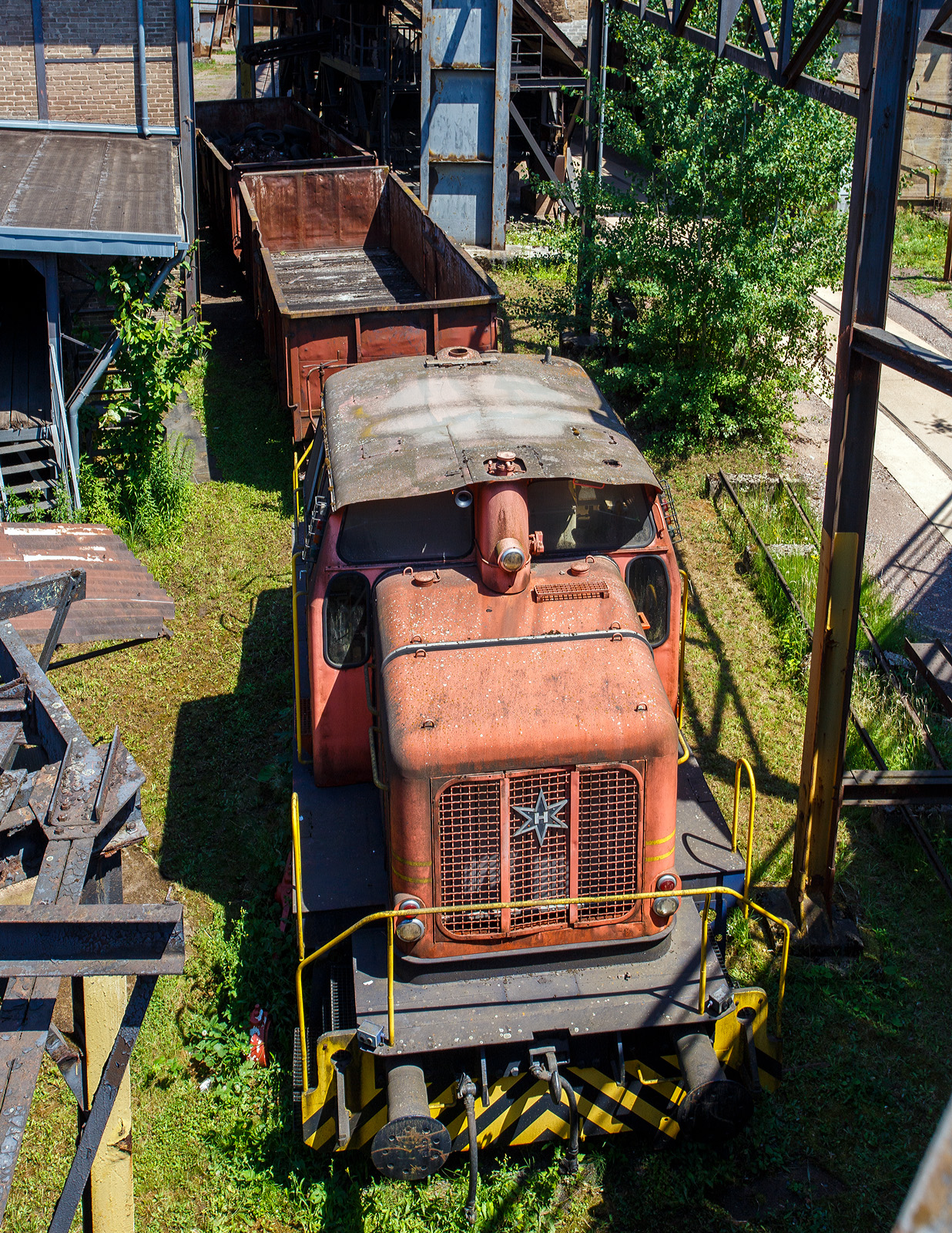 Die ex D V der AG der Dillinger Hüttenwerke (Normalspur – Diesellokomotive 5 /Henschel 29726), eine C-gekuppelte Henschel DH 440 Ca, hier am 01 Juli 2025 als Denkmal ausgestellt im Bereich der Kokssieberei der Völklinger Hütte. 

Die dreifachgekuppelte Lok vom Typ Henschel DH 440 Ca wurde 1959 von der Henschel-Werke GmbH in Kassel unter der Fabriknummer 29726 gebaut und als D V an die AG der Dillinger Hüttenwerke geliefert, wo sie bis 2000 im Dienst war. Die AG der Dillinger Hüttenwerke schenkte 2003 diese Lok dem Weltkulturerbe Völklinger Hütte, heutiger Eigentümer ist die Initiative Völklinger Hütte e.V., diese Lok war nie in Völklingen im Einsatz, aber ähnliche Lokomotiven dieser Bauart werden heute noch im Werksverkehr in Völklingen eingesetzt. Mit solchen Zügen wurden unter anderem Koks zur Kokssieberei transportiert, oder auch Schrottpakete zum Verladen in die Hängebahnwagen. Bei der AG der Dillinger Hüttenwerke sind baugleiche Loks im Werksverkehr in Dillingen im Einsatz. 

Übrigens die AG der Dillinger Hüttenwerke ist heute der einzige Produktionsstandort von Roheisen im Saarland und sie ist das größte Grobblechwerk Europas. Auch wenn die Saarstahl AG mit Anteilseigner ist, so darf man diese gleichsetzen. 

Zu den Loks:
Die Henschel DH 440 Ca sind C-gekuppelte standardisierte Werksbahn-Dieselloks der 3. Generation von Henschel mit dieselhydraulischem Antrieb mittels Kuppelstangen. Die 28 Lok von diesem Typ, mit einem mittelschnell laufenden MAN-Motor, wurden zwischen 1957 und 1965 gebaut. Allein 6 Exemplare wurden an die AG der Dillinger Hüttenwerke geliefert (D V bis D X).

Anders als die DH 440 der 2. Generation hat die DH 440 Ca (der 3. Generation) eine außenliegende Blindwelle (daher auch der Zusatz Ca), es ist auch größte Unterschied. Wobei auch einige Konstruktive Änderungen mitbrachte. 

TECHNISCHE DATEN:
Gebaute Anzahl: 28
Spurweite: 1.435 mm (Normalspur)
Achsformel: C
Lokgewicht: ca. 43 t
Länge über Puffer: 8.900 mm
Fester Radstand: 3.000 mm
Kleinster bef. Halbmesser: 50 m
Höchstgeschwindigkeit:  30 km/h / 60 km/h
Motor: wassergekühlter 8-Zylinder 4-Takt MAN-Dieselmotor mit Aufladung vom Typ MAN W 8 V 17,5/22 A 
Hubraum: 42.320 ccm
Leistung: 324 kW (440 PS)
Nenndrehzahl: 1.100 U/min
Getriebe: Voith L 37 U
Leistungsübertragung: hydraulisch auf Blindwelle, von dieser über Kuppelstangen auf die Räder. 
