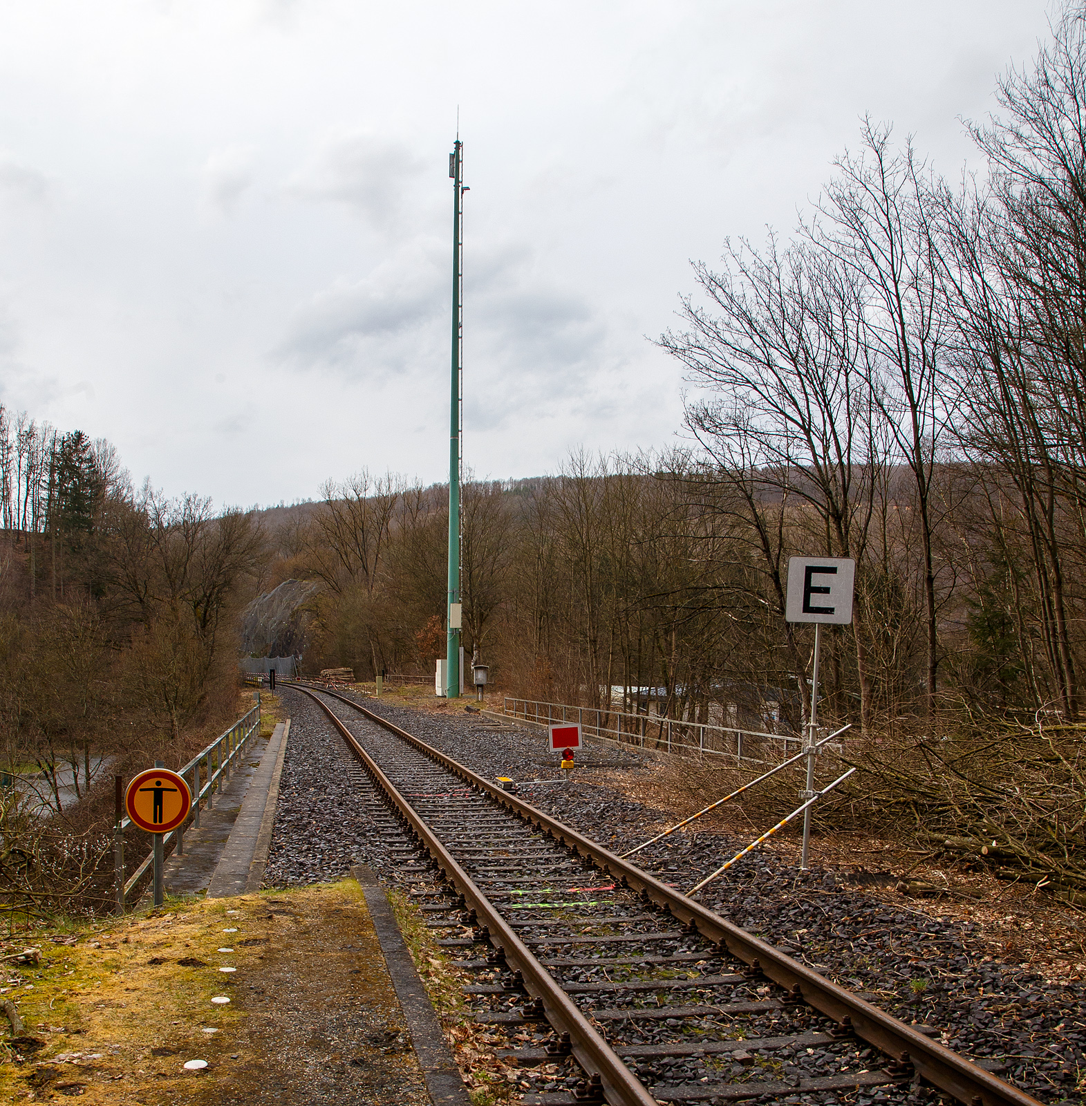 Die Hellertalbahn (KBS 462 / Strecke 2651) bei km 88,4 in Herdorf nahe dem Hp K�nigsstollen am 18.03.2023. Ab den 20.03.2023 sollen die Triebz�ge der RB 96 „Hellertalbahn“, anstelle von Neunkirchen (Siegerland), nun bis zum Hp K�nigsstollen gef�hrt werden. Daf�r wurden Vorbereitungen getroffen.

Vom Bahnhof Herdorf gibt es eine vor�bergehende Langsamfahrstelle (40 km/h). Hier beim Hp K�nigsstollen wurde Lf 3 – Endscheibe gesetzt, diese bedeutet: Ende der vor�bergehenden Langsamfahrstelle (hier 40 km/h). Die Geschwindigkeitsbeschr�nkung in der Langsamfahrstelle ist aufgehoben. Der Lokf�hrer kann wieder auf die Streckengeschwindigkeit beschleunigen. Wobei den Sinn kann ich nicht ganz verstehen, denn ca. 5 m weiter ist ja die Sh 2 - (Schutz-)Halttafel, dieses ist auch bereits durch einen Geber (Sicherungstechnik) abgesichert. 

Ca. 100 m weiter hinten sitzt zudem die neue Gleissperre. Und weiter hinten ist die Gefahrstelle (der Einschnitt) wo es links am 23.12.2022 zu einem Felsstutz kam. Rechts vom Gleis (vom alten 2. Gleis) hatten bereits umfangreiche Hangsicherungsma�nahmen stattgefunden. Hatte da vielleicht damals jemand die Seiten vertauscht;-)


