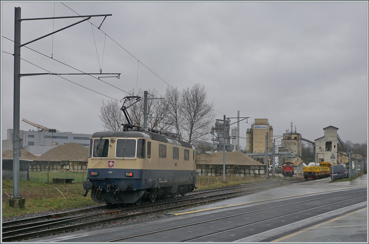 Die von Morges gekommene IRSI/IGE  Rheingold  Re 4/4 II 11387 (Re 421 387-2) hat in Gland die Strecke nach Gen�ve verlassen und f�hrt nun �ber ein Industriegleis in Richtung Kieswerk, um dort ihren Zug nach Apples abzuholen. 
Die angemietete IRSI/IGE Re 4/4 II 11387 (Re 421 387-2) ersetzt die zur Zeit in der Revision in Bellinzona weilende BAM MBC MBC Re 420 506. 

22. Feb. 2024