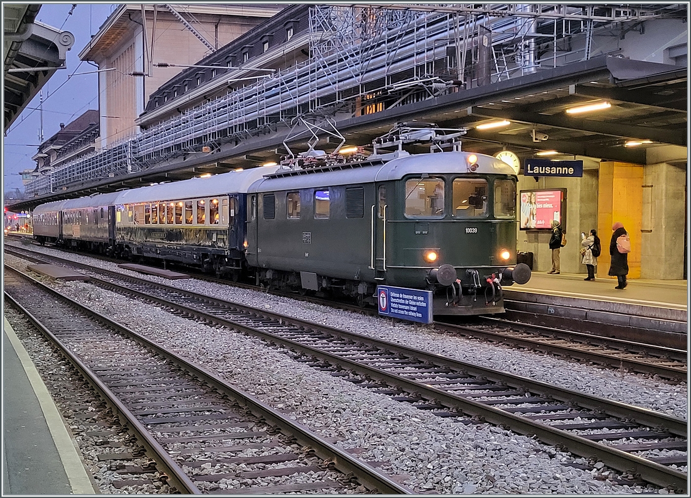 Die Re 4/4 I 10039 stellt den Extrazug 31131 in Lausanne bereit. Der Zug verkehrt f�r eine Reisegruppe nach Z�rich Enge (mit Halt in Pal�zieux). Der Zug besteht aus dem  Le Salon Bleu  61 85 80-90 200-6 CH-IRSI, dem 56 80 89-80 010-2 WGm D-IRSI und dem Am 56 80 10-40 360-4 D-IRSI. Da der TEE Rheingold Gen�ve - Amsterdam am Schluss seiner Einsatzzeit vor vielen Jahren aus einem DB Speisewagen, einem DB Abteilwagen und einen DB Gro�raumwagen bestand und auch von einer Re 4/4 I gezogen wurde, weckt der heutige Zug doch Erinnerungen an den TEE 6 / 7, der am 23. Mai 1982 zum letzten Mal ab Gen�ve fuhr, (und sich dann noch gut zwei Jahre auf dem Abschnitt Basel - Amsterdam hielt). Leider die Re 4/4 I 10039 etwas ungeschickt vor dem Schild  �berschreiten der Geleise verboten, und leider waren diese Lichtverh�ltnisse nichts f�r meine kleine Knipse, so dass ich hier ausnahmsweise ein Handy-Bild zeige. 
Die Re 4/4 I geh�rt heute der SWISS RAIL TRAFFIC und war fr�her als Re 416 628 bei der Mittelthurgaubahn unterwegs und vorg�ngig bei den SBB mit der heute noch angeschrieben Nummer 10039 im Einsatz. Damals trug die am 22. Dez. 1950 abgelieferte Lok jedoch noch die verchromten Buchstaben SBB - CFF resp. SBB - FFS an den Seitenw�nden.

11. Dezember 2024