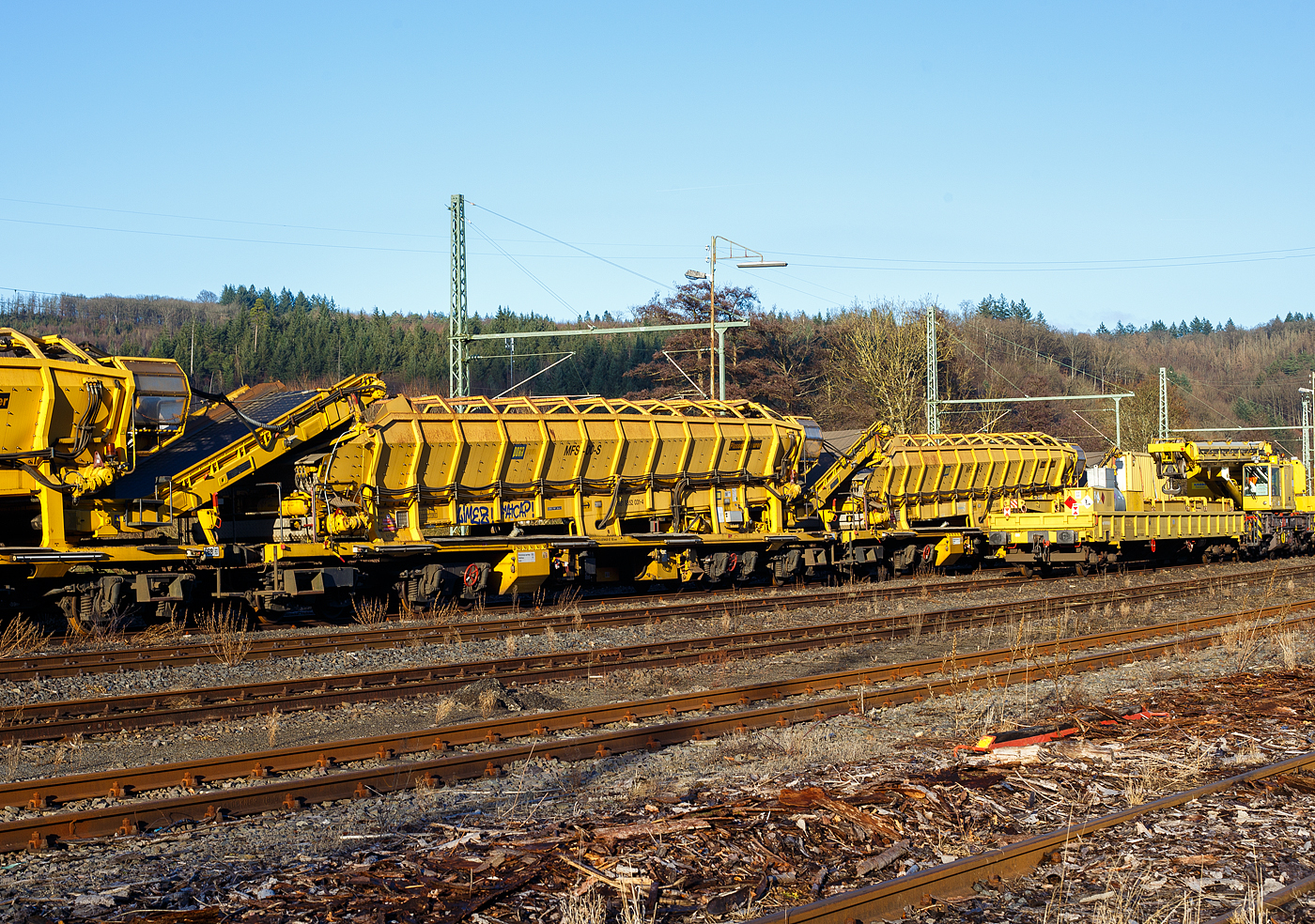 Drei Plasser & Theurer Materialf�rder- und Siloeinheiten (MFS 100) der �sterreichischen Gleisbaufirme PORR AG (Wien) sind, mit einem Schutzwagen, am 26 Dezember 2024, in Scheuerfeld/Sieg abgestellt. Hier im Vordergrund die P&T Materialf�rder- und Siloeinheit MFS 100 S (mit Endladung nach unten ins Gleis m�glich) 99 81 9352 031-4 A-PTU.

TECHNISCHE DATEN:
Hersteller: Plasser & Theurer, Linz an der Donau (�sterreich)
Spurweite: 1.435 mm
L�nge �ber Puffer: 22.900 mm
Achsanzahl: 8 (in 2 Doppel-Drehgestellen)
Drehzapfenabstand der Doppeldrehgestelle: 15.100 mm
Drehzapfenabstand der Einzeldrehgestelle: 3.900 mm Achsabstand der Einzeldrehgestelle: 1.500 mm
Motorleistung: 165 kW (wassergek�hlter Deutz BF6M 1013 C Motor f�r Bandantrieb)
Eigengewicht: 64 t
Nutzlast: 80 t ab D4
Fahrgeschwindigkeit in Schleppfahrt leer, max.: 120 km/h
Fahrgeschwindigkeit in Schleppfahrt beladen, max.:100 km/h
Fassungsverm�gen: 68 m�
F�rderleistung (materialabh�ngig), max.: 700 – 800 m�/h
Entladezeit: ca. 5 min
