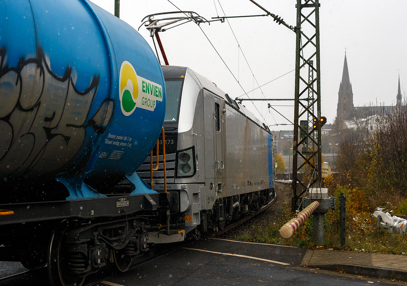 Eigentlich war ich auf die Ausfahrt von dem RE 9 am 22 November 2024 bei Schneefall aus Bahnhof Kirchen/Sieg fokussiert auch die Sicht in die Gegenrichtung war durchs Schalthaus vom Bü verdeckt, so schlich sich die fast fabrikneue SIEMENS Vectron MS 6193 173 (91 80 6193 173-2 D-Rpool) der Railpool mit einem Kesselwagenzug in Richtung Siegen heran. Daher war hier nur noch der Nachschuss möglich. Daher kann ich manchmal die Diskussionen über Bahnlärm nicht verstehe, den Güterzug konnte ich nur auf den letzten Metern hören. 

Die SIEMENS Vectron MS wurde 2024 von SIEMENS Mobilitiy in München-Allach unter der Fabriknummer 23499 gebaut.