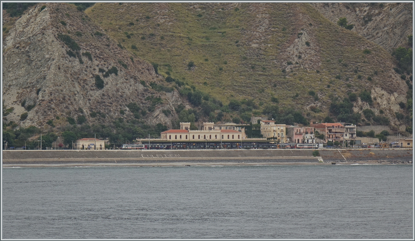 Ein Blick auf den Bahnhof Taormina Gardini vom Meer her: Während der interCity notte 1959 von Roma Termini nach Siracusa im Bahnhof kurz hält,  verdeckt   ein dort abgestellter FS Treniatlia ETR 104 (Coradia Stream Pop) die Sicht auf den Nachtzug. 

24. Sept. 2025