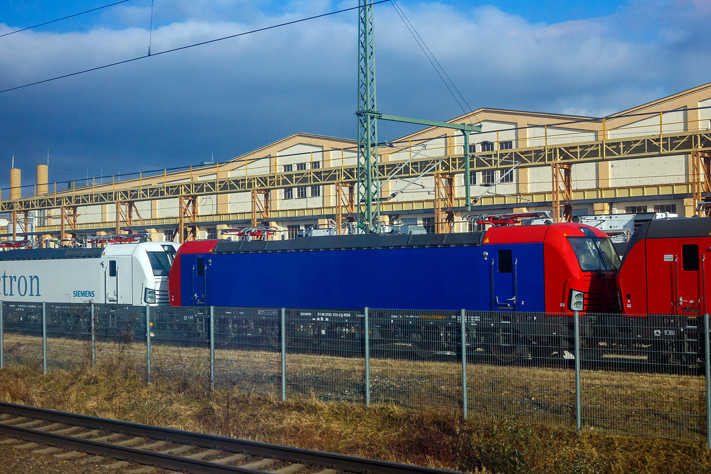 Frisch aus der Produktion, noch nicht ausgeliefert und noch ohne SBB Cargo AG Werbung, die SIEMENS Vectron AC – 193 070-0 (91 80 6193 070-0 D-RCM) f�r die RCM Rail Care and Management GmbH (M�nchen), steht am 13 Januar 2025 auf dem Werksgleisen vor den Werkshallen der SIEMENS Mobilitiy in M�nchen-Allach. Aufnahme aus einem ICE heraus.

Die Wechselstromlok (AC 15 kV 16,7 Hz und AC 25 kV 50 Hz) vom Typ SIEMENS Vectron AC wurde 2024 von Siemens Mobilitiy in M�nchen-Allach unter der Fabriknummer 23692 gebaut. Sie wurde in der Variante Vectron AC B48 ausgef�hrt und hat so die D / A / CH Zulassungen (Deutschland, �sterreich und die Schweiz). Diese Vectron AC B48 besitzen auch nur 2 Stromabnehmer, jeweils einen mit breiter und schmaler Wippe. Im M�rz 2025 wurde die Lok an die LokRoll3 AG, Luzern (eingestellt �ber die Rail Care and Management GmbH, Starnberg) geliefert und von dieser, f�r die n�chsten 8 Jahre, an die SBB Cargo AG vermietet.

