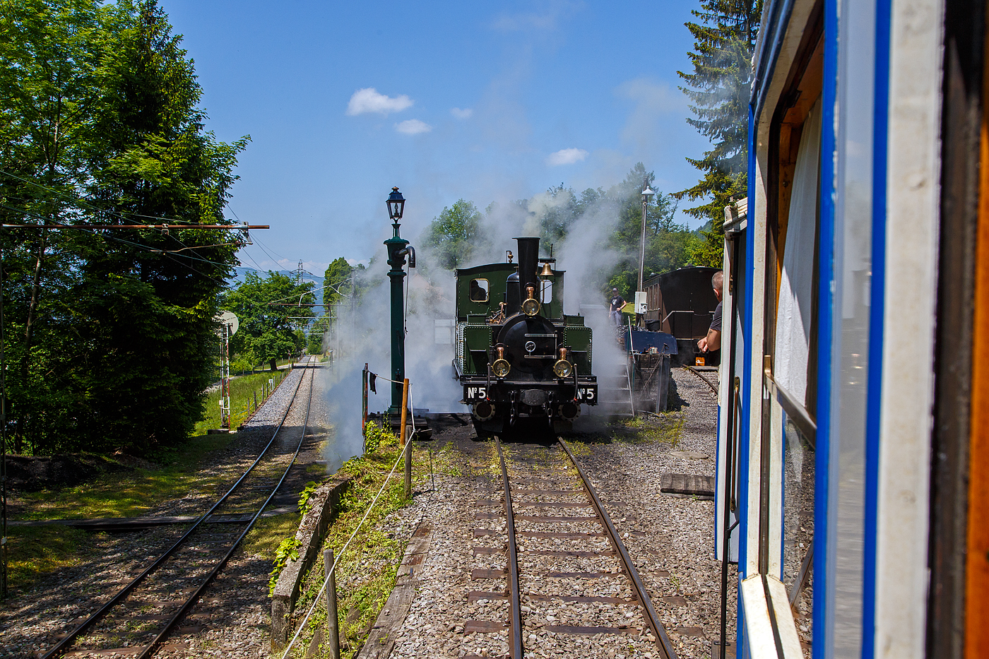 Museumsbahn-Romantik pur – Pfingsten 2023 (Samstag 27. bis Montag 29. Mai 2023) fand bei der Museumsbahn Blonay–Chamby das Schweizer Dampffestival 2023 / Festival suisse de la Vapeur 2023 statt.

Bei der Dampflok-Wartungsstelle der Museumsbahn Blonay–Chamby beim Museumsareal in Chaulin steht am 27.05. 2023 die G 3/3 LEB N° 5  Bercher  der Museumsbahn zum Kohlefassen. Links die Strecke 115 der MVR hinab nach Blonay, wir fahren mit dem ex MOB BCFe 4/4 11 rechts das Stichgleis zum Museum bzw. Depot hinauf.

Die ex LEB Nr. 5  Bercher  (Lausanne–Echallens–Bercher-Bahn) wurde 1890 von der Elsässische Maschinenbau-Gesellschaft Grafenstaden (später Société Alsacienne de Constructions Mécaniques) unter der Fabriknummer 4172 gebaut und an die Lausanne–Echallens–Bercher-Bahn geliefert. Die EMBG hatte auch zwei Jahre zuvor die baugleiche Nr. 2 geliefert. Die beiden dreiachsigen Tenderlokomotiven trugen die Hauptlast des Verkehrs, bis in den Jahren 1903 und 1905 zwei baugleichen Tenderlokomotiven, die G 3/3 6 „Gros-de-Vaud“ und G 3/3 7 „Talent „durch die Schweizerische Lokomotiv- und Maschinenfabrik (SLM) in Winterthur abgeliefert wurden. 

Von der YSteC konnte die LEB 1920/1921 die drei 1893 ebenfalls durch die EMBG gebauten Mallet-Lokomotiven G 2x2/2 Nr. 1 bis 3 gebraucht übernehmen. Nun waren die G 3/3 Nr. 2 und 5 nicht mehr gefragt. Während die G 3/3 2 „Échallens“ bereits 1929 verschrottet wurde (seit 1920 war sie bereits abgestellt), die G 3/3 Nr. 5  Bercher  hatte es da etwas besser, sie wurde 1934 an die Firma Energie de l’Ouest Suisse (EOS) für die Baustelle der Staumauer Grande-Dixence verkauf. Nach dem die Arbeiten 1935 erledigt sind geht sie bei der EOS außer Betrieb. Im Jahr 1939 verlässt die Schweiz und geht nach Vorarlberg in Österreich, zu einer Baufirma. Die Baufirma verschenkte 1967 die Lok und sie wurde, wie viele andere Dampflokomotiven zu dieser Zeit, auf einem Kinderspielplatz in der Stadt Feldkirch aufgestellt. Das Ausstellungsobjekt weckte die Aufmerksamkeit einiger Mitarbeiter der Museumsbahn Blonay–Chamby (BC), denen es gelang 1973 diese Lokomotive im Tausch gegen eine andere Lok zu erwerben.

Nach einer Aufarbeitung war die Lokomotive 1985 bis 2005 in Betrieb. Dann musste sie abgestellt werden. 2013/2014 wurde die Lokomotive ein zweites Mal durch die Museumseisenbahner aufgearbeitet. Seit dem Frühling 2015 ist die zweitälteste Schmalspur-Dampflokomotive der Schweiz, die älteste ist die G 3/4 1 „Rhätia  der Rhätischen Bahn (RhB), nach dem Abschluss der Revisionsarbeiten wieder in Betrieb.

TECHNISCHE DATEN der LEB G 3/3 N° 5  Bercher :
Baujahr: 1890
Spurweite: 1.000 mm
Achsformel: C
Länge über Puffer: 6.830 mm
Achsabstand: 1.800 mm (950mm / 850 mm)
Dienstgewicht: 20,4 t
Anzahl der Zylinder: 2
Zylindergröße: Ø 270 mm x 370 mm Kolbenhub
Treibraddurchmesser: 810 mm
Höchstgeschwindigkeit: 25 km/h
Stundenleistung: 150 PS
Kesselüberdruck: 12 bar
Kohlevorrat: 0,8 t
Wasservorrat: 2,2 m³

Die Lausanne–Echallens–Bercher-Bahn, abgekürzt LEB, französisch Chemin de fer Lausanne–Echallens–Bercher, ist eine meterspurige Privatbahn. Die knapp 24 Kilometer lange Strecke führt vom Stadtzentrum von Lausanne (Flon) durch die nördlichen Vororte und weiter nach Echallens und Bercher im Gros de Vaud, dem Waadtländer Hinterland. Die LEB ist eine moderne Vorortbahn, die in Lausanne teilweise unterirdisch verkehrt. Die Züge fahren alle 30 Minuten (zwischen Echallens und Bercher gibt es einige wenige Taktlücken am Vormittag). Werktags wird ein Viertelstundentakt bis Cheseaux angeboten. Von Montag bis Freitag verkehren in Lastrichtung einige beschleunigte Hauptverkehrszüge.