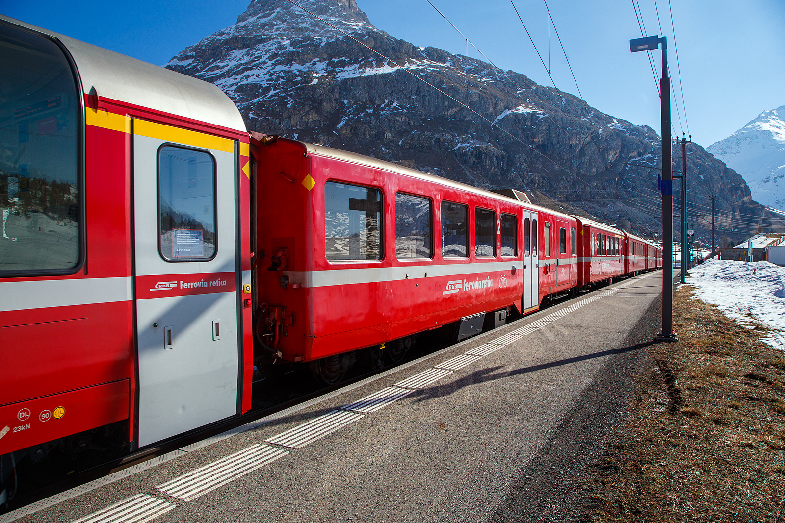 RhB Berninabahn Velowagen, ein verk�rzter 2.Klasse Mitteleinstiegswagen mit Gep�ckabteil in leichter StahlbauartRhB WS 3931, ex RhB BD 2477, ex RhB B 2334, ex B4� 2334, am 22.03.2023 in der Station Bernina Diavolezza (2.082 m �. M.) im Zugverbund. Wegen der Steckengeometrie, mit Radien von teils nur 50 m, m�ssen auf der Berninalinie k�rzer Wagen, als auf dem Stammnetz, eingesetzt werden.

Am 13.09.2017 konnte ich ihn noch als BD 2477 in Ospizio Bernina ablichten, siehe http://hellertal.startbilder.de/bild/schweiz~wagen~personenwagen-rhb-schmalspur/644168/rhb-bd-2477-ein-verkuerzter-2klasse.html

1956 bis 1957, kurz nach Abschaffung der dritten Klasse, erhielt die RhB noch einmal 13 Leichtstahlwagen. Diesmal kamen die Wagen von SIG Neuhausen und wiesen aber viele Gemeinsamkeiten mit den Leichtmetallwagen fr�herer Bauart auf: Fl�gelt�ren, WC beim Mitteleinstieg, Stirnwandt�ren direkt im Personenabteil, gleicher Sitzteiler. Die Wagen waren aber 18.26 m lang, liefen auf SIG-Torsionsstab-Drehgestellen (System Frei). Die Wagen erfuhren verschiedene Umbauten zu Steuerwagen (BDt 1731), Pendelzugwagen, Velowagen und verk�rzten Wagen (BD 2477–2478) f�r die Berninalinie. Dabei erhielten sie au�en b�ndige Schwenkt�ren.

Dieser Wagen wurde 1956 gebaut als B4� 2334 geliefert, sp�ter in B 2334 umgezeichnet. Im Jahr 2003 f�r den Einsatz auf der Berninabahn verk�rzt und zum 2.Klasse Wagen mit Gep�ckabteil umgebaut, 2019 erfolgte ein weitere Umbau zum heutigen Velowagen WS 3931, wobei wie hier im Winter dient er als Skiwagen.

TECHNISCHE DATEN:
Baujahr und Hersteller: 1956 - SIG
Spurweite: 1.000 mm
Anzahl der Achsen: 4
L�nge �ber Puffer: 16.220 mm
Drehgestellart: SIG Torsionsstab
Sitzpl�tze: 30
Eigengewicht: 19,0 t
Ladefl�che: 9 m�
Ladegewicht: 2,0 t
Max. Gesamtgewicht: 25 t
zul�ssige Geschwindigkeit: 90 km/h
Lauff�hig: StN (Stammnetz) / BB (Berniabahn) / MGB (Matterhorn Gotthard Bahn)
