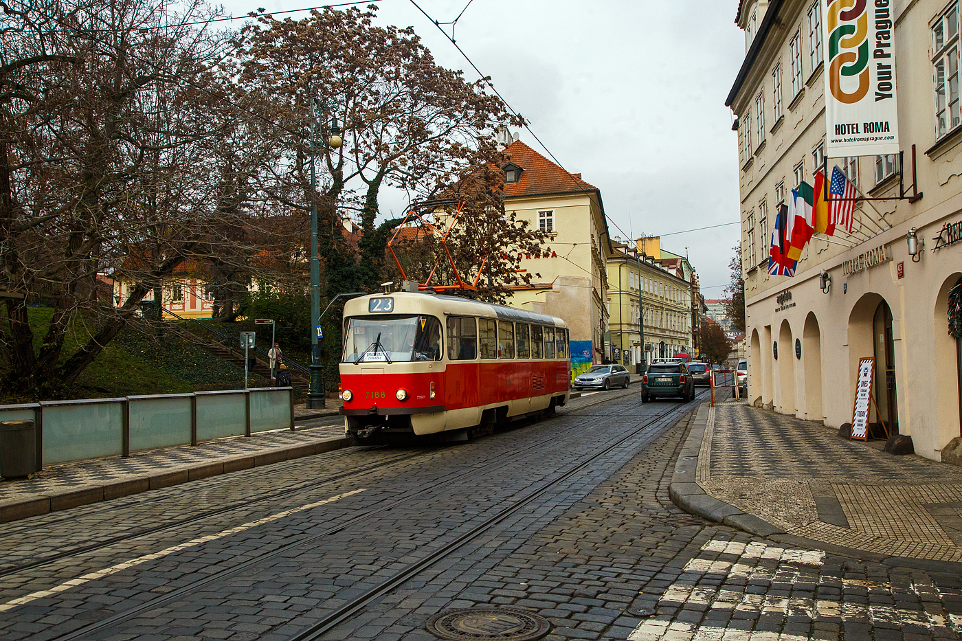 Stra�enbahn Prag, der Triebwagen DPP 7188 erreicht, als sog. nostalgische Linie 23 (Kr�lovka – Malostransk� – N�rodn� divadlo – Zvonařka) am 23.11.2022 die Station �jezd (�jezd / Praha). Links sieht man auch die Talstation �jezd der Petř�n-Standseilbahn.

Der Triebwagen ist ein ČKD Tatra T3 SUCS, er wurde 1986 von ČKD Tatra in Prag unter Fabriknummer 175 352 gebaut. 

ČKD Tatra T3 SUCS:
Da bereits ab Ende der 1970er Jahre in gr��erem Umfang etliche Wagen vom Typ T1 verschrottet wurden und auch der restliche Wagenpark von diesem Typ schon das Ende erreicht hatte, mussten dringend neue Fahrzeuge f�r Prag her. Es war Anfang der 1980er Jahre geplant den neuen Gelenkwagentyp in gr��eren St�ckzahlen zu bestellen. Da dieser aber immer noch nicht zur Verf�gung stand und zum anderen die Produktion der alten Wagen vom Typ T3 Ende 1976 auslief, fanden Verhandlungen mit dem CKD-Tatra Werken �ber neue Fahrzeuge die kurzfristig lieferbar w�ren statt. Da die Technik der Thyristortechnik (TV1) schon veraltet war und nur mit teurem Aufwand zum Einbau gekommen w�re, entschied man sich f�r den Bau der Exportversion vom Typ T3SU. Dieser Wagentyp hatte aber wieder den herk�mmlichen PCC-Beschleuniger als Steuerung. Besonderheiten gegen�ber dem bisherigen T3 war die Serienm��ig ausgestattete geschlossene Fahrerkabine, mehr Sitzpl�tze und der Dachaufstieg befindet sich nun an der hinteren T�r (beim T3 mittlere T�r). Da die Wagen vom Typ T3SU und T3SUCS die gleiche Vielfachsteuerung hatten wie die vom Typ T3 konnten sie auch mit dem Typ T3 in Traktion gefahren werden. Die ersten 20 Wagen (7001 - 7020) hatten eine 2+1 Bestuhlung im Fahrgastraum, weshalb sie auch Typenm��ig als T3SU bezeichnet wurden. Ab dem Wagen 7021 besa�en alle weiteren Wagen die typische 1+1 Bestuhlung und wurden als T3SUCS bezeichnet.
