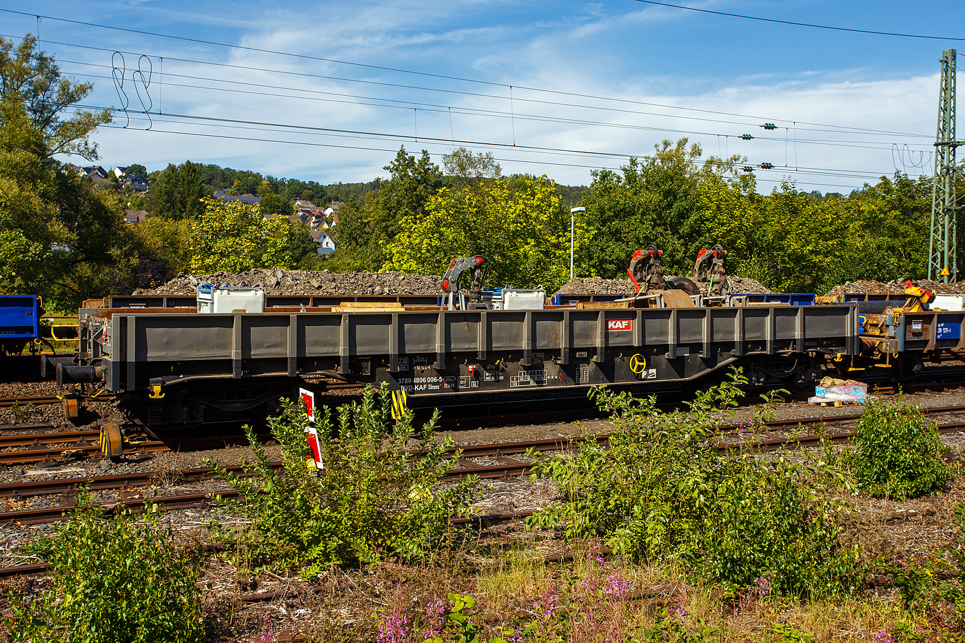 Vierachsiger Drehgestell-Flachwagen, mit festen Seitenwänden und Stirnwandklappen, 37 80 4806 006-5 D-KAF, der Gattung Slmns1, der KAF - Falkenhahn Bau AG (Kreuztal), beladen mit Material und Equipment für die Baustelle, abgestellt am 26 August 2025 im Zugverband in Scheuerfeld/Sieg nahe der Baustelle. 

TECHNISCHE DATEN:
Spurweite: 1.435 mm (Normalspur)
Gattung/Bauart: Slmns1
Anzahl der Achsen: 4 in 2 Drehgestellen
Länge über Puffer: 16.740 mm
Drehzapfenabstand:  11.700 mm
Achsabstand in den Drehgestellen: 1.800 mm
Eigengewicht: 23.900 kg
Ladelänge: 15.500 mm
Ladefläche: 43,3 m²
Maximale Ladegewicht: 66,1 t (Streckenklasse D)
Höchstgeschwindigkeit: 100 km/h (beladen) / 120 km/h (leer)
Kleinster befahrbarer Gleisbogenhalbmesser: R 45 m
Feststellbremse: ja
Bauart der Bremse: KE-GP-A (K), Max. 58 t
Bremssohle: C 810
Intern. Verwendungsfähigkeit: TEN-GE / G1

Bedeutung der Gattungsbezeichnung (Slmns):
S = Flachwagen mit Drehgestellen in Sonderbauart
l = ohne Rungen
m = mit vier Radsätzen, Ladelänge 15 m bis unter 18 m
n = mit vier Radsätzen höchste Lastgrenze über 60
s = lauffähig (beladen) bis 100 km/h

Quelle: laut Anschriften