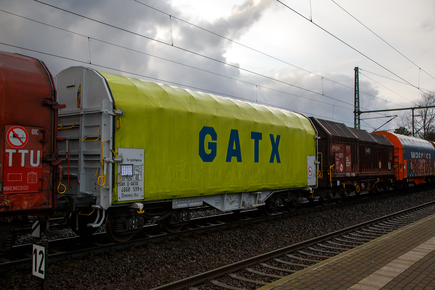 Vierachsiger Drehgestell-Flachwagen mit verschiebbarem Planenverdeck und Lademulden für Coiltransporte, 37 80 4668 599-6 D-GATED, der Gattung Shimmns-ttu, der GATX Rail Germany GmbH, am 07.12.2022 im Zugverband bei einer Zugdurchfahrt im Bahnhof Dresden-Strehlen. Der Waggonvermieter GATX (General American Transportation Corporation) ist eine US-amerikanische Leasinggesellschaft für Schienenfahrzeuge mit Sitz in Chicago. GATX wurde 1898 gegründet und ist seit 1916 an der New Yorker Börse notiert.

Diese Wagen sind speziell für den Transport witterungsempfindlicher Blechrollen (Coils) bestimmt. Er besitzt feste Stirnwände, 5 fest im Untergestell eingebaute Lademulden. Die Wagenabdeckung erfolgt mit einer PVC-beschichteten Gewebeplane, die auf 11 Rohrrahmen aufliegt. Über Laufwagen ist das Planendach in Wagenlängsrichtung verschiebbar. Die Verriegelung des Planendaches an den Stirnwänden erfolgt über eine 4-Punkt-Zentralverriegelung, die sowohl vom Erdboden als auch von der Rampe aus bedient werden kann. Das Planenverdeck lässt sich an einem Wagenende so weit zusammenschieben, dass ca. 2/3 der Ladefläche zur Beladung freigegeben wird. Hierdurch ist eine einfache Beladung des Wagens sowohl von oben als auch von der Seite aus möglich. 

TECHNISCHE DATEN:
Spurweite: 1.435 mm
Achsanzahl: 4 (in 2 Drehgestelle)
Länge über Puffer: 12.040 mm
Länge der Ladefläche: 10.800 mm
Drehzapfenabstand: 7.000 mm
Achsabstand im Drehgestell: 1.800 mm
Eigengewicht:  21.770 kg
Höchstgeschwindigkeit: 100  km/h (beladen) / 120 km/h (leer)
Maximales Ladegewicht: 68,2 t (Streckenklasse D4)
Kleinster bef. Gleisbogenradius: 35 m
Bauart der Bremse: KE-GP-A (K)
Bremssohle: C 810
Intern. Verwendungsfähigkeit: TEN - GE