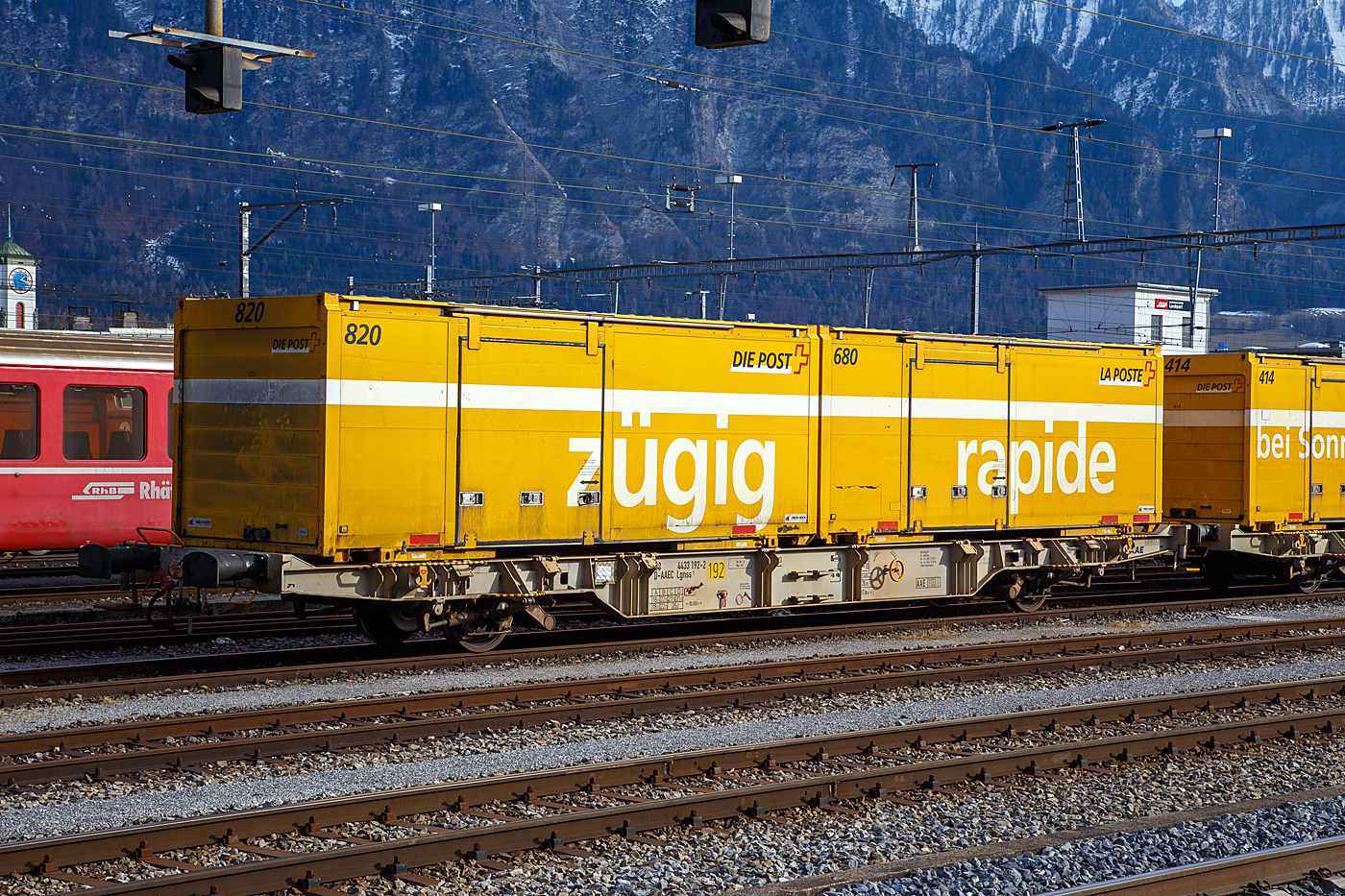 Zweiachsiger Behältertragwagen 43 68 4433 192-2 D-AAEC, der Gattung Lgnss 1 der ehemaligen AAE Ahaus-Alstätter Eisenbahn Cargo AG mit Sitz in Baar (2015 zur VTG AG, Hamburg) vermietet an die Schweizerische Post AG, beladen mit zwei Wechselbrücke (WB) am 20 Februar 2017 abgestellt im Bahnhof Landquart.

Die Schweizerische Post AG (ex PTT) betreibt für den schweizweiten Brief- und Paketversand, aber auch Stückgutlogistik von palettisierte Handelswaren, Rohstoffen oder Gefahrgut andere Kunden, einen Kombiverkehr von Tür zu Tür. Die Post verlädt die Waren von der Straße auf die Schiene und liefert sie an die gewünschte Adresse in Post eigenen oder Kunden Wechselbehälter oder Containern. Für die Wechselbehälter oder Container gibt es Umschlagsterminals der Post in Daillens, Härkingen, Frauenfeld, Landquart oder Cadenazzo.

Um den schweizweiten Brief- und Paketversand schneller und letztlich auch wirtschaftlicher zu gestalten, investierte die Schweizer Post massiv in den Aufbau einer Logistik, die den Wechselbehälter als tragendes Element vorsieht. Um auch die Eisenbahn in dieses System einzubeziehen und nicht, wie in vielen anderen Ländern geschehen, nahezu ausschließlich auf die Straße als Verkehrsträger zu setzen, musste ein geeigneter Tragwagen gefunden werden.
Die Rollmaterialknappheit im Kombinierten Verkehr ist jedoch so alt wie der KV selbst. Zudem hatte es Ende der 1990er Jahre kaum für das Anforderungsprofil geeignete Waggons. Immerhin sollten je Waggon zwei Behälter (WB) transportiert werden können. Vierachsige Waggons waren hierzu eindeutig 
überdimensioniert und wären durch viel ungenutzte Ladelänge sowie großer »Totlast« unwirtschaftlich gewesen. Die meisten Vierachser sind ausgelegt für 60' Ladelänge und somit gut geeignet für ISO-Container,  nicht jedoch für die Wechselbrücken, deren Längenmaße zwischen 23,5' (7,15m) und knapp 26' (7,82m) liegen.

Zweiachsige Waggons wurden jedoch wseit den 1980er Jahren europaweit kaum noch neu gebaut, da sie für den Containertransport aufgrund der maximalen Achslast nur begrenzt nutzbar sind. Zudem sorgten auch unerfreuliche Vorfälle von Entgleisungen im Rangierbetrieb solcher Waggons mit langem Achsstand für eine Abkehr vom Zweiachser. Während die UIC maximal 9 m vorsieht, lassen sich Ladelängen für Wechselbehälter oft nur mit 10 m Achsstand realisieren. Damit war klar, dass für den geplanten Einsatz nur eine Neukonstruktion in Frage kam.

So beauftragte die Schweizer Post die Ahaus-Alstätter-Eisenbahn (AAE) in Baar, damals einer der größten Waggonvermieter Europas (gehört seit 2015 zur VTG AG) mit Konstruktion und Lieferung eines geeigneten Waggons, der dann langfristig von der Post angemietet werden sollte. Die AAE ließ daraufhin bei MSV Studenka (Tschechische Republik) einen zweiachsigen Behältertragwagen bauen, der mit einem Radstand von 10 m eine Ladelänge von 15 m aufweist und somit geeignet für das geforderte Beladungsszenario von zwei 7,45m Wechselbehältern (C745) ist.

Der Wagenrahmen besteht aus einer geschweißten Stahlkonstruktion mit außenliegenden fischbauchartigen Längsträgern in Doppel-T-Profil. Weiterer wichtiger Aspekt war, die Konstruktion nicht nur lauf-, sondern auch bremstechnisch für ss-Verkehre (HG 120 Km/h) auszulegen. Lauftechnisch wird dieses erreicht durch Einsatz von zwei längseingebauten Wende- sowie vier Querdämpfern zwischen Radsatzlagern und Wagenrahmen. Bremsseitig verfügt der Waggon über eine selbsttätig lastabhängig wirkende Druckluftbremse. Die Bremskraft wird dabei über jeweils zwei Aluminiumkeramik-Bremsscheiben pro Achse übertragen. Die Anbringung der Bremszangen an zwei massiven, querliegenden Rohrkonstruktionen verleiht dem »Postwagen«, zusammen mit Dämpfern und Fischbauchträgern, sein charakteristisches Aussehen.

Die Ladeflächenhöhe liegt durchgehend bei 1.070 mm über SO und unterschreitet somit die gemäß UIC-Merkblatt 571-4 (Einheitsgüterwagen – Güterwagen des kombinierten Verkehrs) vorgesehene Normalhöhe um 100 mm. Bei einem Eigengewicht von 14 t weist der »Postwagen« eine für den Einsatzzweck in der Brief- und Paketlogistik geeignete Lastgrenze von 26 t (ss-Verkehre) resp. 31t (s) auf. Das Maximalgewicht des Wagens liegt somit bei 45 t, im Betrieb werden 31,6 t als Normgewicht angesetzt (die Ladeinheiten werden im Post-Betrieb nicht verwogen!).

Trotz zusätzlich an den Wagenenden eingebauter Schwingungsdämpfer, die Schwingungen der Waggonstruktur bei teilbeladenen Waggons verhindern sollen, verkehren die »Postwagen« entweder leer oder immer mit zwei Behältern beladen, selbst wenn einer davon leer mitgeführt wird.

Inklusive drei Prototypen wurden 1999 in gesamt 253 Wagen gebaut und bei der AAE in Dienst gestellt. Alle Einheiten sind in RAL 7044 seidengrau lackiert. Als zweiachsiger Tragwagen trägt der »Postwagen« die Bauartbezeichnung Lgnss und ist gemäß UIC 438-2 (Kennzeichnungen der Güterwagen) eingereiht als (43 68) 4433 000 – 252. Die Kennzeichnung 43 verweist dabei auf die nicht vorhandene RIV-Kompatibilität, da der Wagen nur innerhalb der Schweiz eingesetzt wird, aber eingestellt sin sie in Deutschland.

TECHNISCHE DATEN:
Gattung: Lgnss 1
Spurweite: 1.435 mm (Normalspur)
Anzahl der Achsen: 2
Länge über Puffer : 17.300 mm
Achsabstand: 10.000 mm
Ladelänge : 15.000 mm (zwei Wechselbehälter [C745] 7,45 m lang)
Ladehöhe über SOK: 1.070  mm 
Max. Zuladung bei Lastgrenze S: 31,0 t (ab Streckenklasse D)
Max. Zuladung bei Lastgrenze SS: 26,0 t (ab Streckenklasse C)
Max. Geschwindigkeit: 100 km/h (Lastgrenze S) / 120 km/h (bei Lastgrenze SS oder leer)
Eigengewicht: 13.600 kg
Bremse: DK-GP-A (D)
Handbremse: Ja
Verwendungsfähigkeit: Nur Schweiz

Quelle: kombimodell.waggonfabrik.eu, Schweizerische Post AG und eigene Sichtung der Anschriften 
