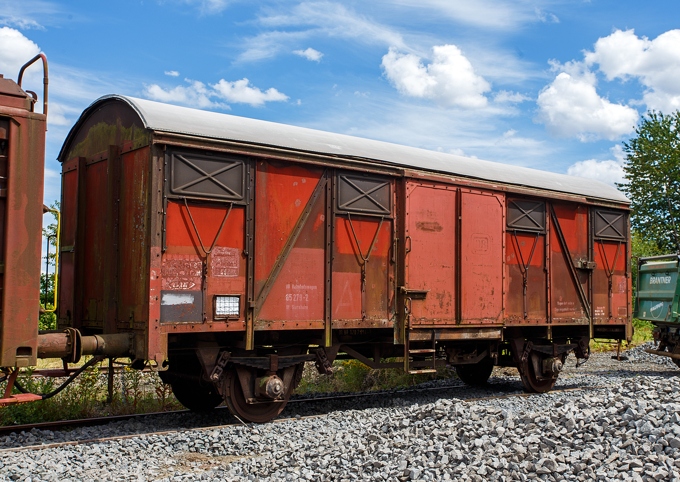 Zweiachsiger gedeckter Güterwagen als DB Bfwg 65 279-2 Bf Siershahn (DB Bahnhofswagen), ehem. zweiachsiger gedeckter Güterwagen 01 RIV-EUROP 80 DB 120 7 614-9, der Gattung Gs 210, ausgestellt am 07 Juli 2024 beim Erlebnisbahnhof Westerwald der Westerwälder Eisenbahnfreunde 44 508 e. V. in Westerburg, hier war Lokschuppenfest.

TECHNISCHE DATEN als Gs 210:
Spurweite: 1.435mm
Achsanzahl: 2
Länge über Puffer:  11.080 mm
Radsatzstand:  5.700 mm
Ladelänge:  9.280 mm
Ladebreite:  2.710 mm
Ladefläche:  25,2 m²
Laderaum:  64,0 m³
Türöffnung (B × H):  2.000 × 2.000 mm
Höchstgeschwindigkeit: 100 km/h
Kleinster bef. Gleisbogenradius:  35  m
Bauart der Bremse:  KE-GP
Austauschverfahren:  01
Intern. Verwendungsfähigkeit:  RIV-EUROP

Der Internationale Eisenbahnverband (Union internationale des chemins de fer, UIC) gründete im Jahre 1949 eine eigene Forschungs- und Entwicklungsanstalt (ORE) und legte damit den Grundstein für international gültige Baugrundsätze von Güterwagen. Auf den ausgearbeiteten Entwürfen und Grundlagen der ORE für einen zweiachsigen Standard Güterwagen, entwickelten die Europäischen Bahnverwaltungen alsbald Ihre eigenen Fahrzeuge. Diese konnten dem Grundgedanken des UIC entsprechend, innerhalb der Gebiete der Mitgliedsverwaltungen zum Transport von Waren und Gütern eingesetzt werden. Die Deutsche Bundesbahn machte mit den ersten rund 3.500 Wagen (nach den vorläufigen Entwürfen) den Anfang und konnte bereits ab 1957 mit dem Gmm(e)hs 56 die ersten 2.662 echten UIC-Standardwagen in Betrieb nehmen. Äußerlich wurde die standardisierte Bauart durch die Anschrift RIV St UIC kenntlich gemacht. Andere Bahnverwaltungen wie die SNCF, FS, ÖBB, NS, DSB, MAV, P.K.P., CFL, SBB agierten in ähnlicher Art und Weise und fertigten ihre eigenen Ausführungen der UIC-Standardwagen. Durch diesen Umstand sind sich die Wagen alle sehr ähnlich, weisen aber zudem immer wieder länderspezifische Bauartunterschiede auf. Da die DB selbst einen sehr großen Bedarf an neuen Wagen hatte und es zudem bei älteren Wagengattungen einen Modernisierungsstau gab, kam es nicht nur zum Komplettneubau von UIC St Wagen. In mehreren Umbauprogrammen, bei denen einzelne Teile älterer Wagen wiederverwendet wurden, entstanden nach und nach die Wagenbauarten Gmms 44, Gmm(eh)s 60, Gmms 40 sowie 216. Für die 1960er bis 1990er Jahre waren diese Wagenbauarten prägend für den Güterverkehr in Europa und mit über 100.000 gebauten Stück in fast jedem Güterzug eingereiht.
