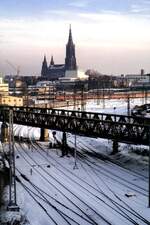 Bahngelände in Ulm mit Ulmer Münster, im Hintergrund fährt eine 111 mit dem ÖBB EC Mozart in Richtung Stuttgart aus, am 07.12.1980.